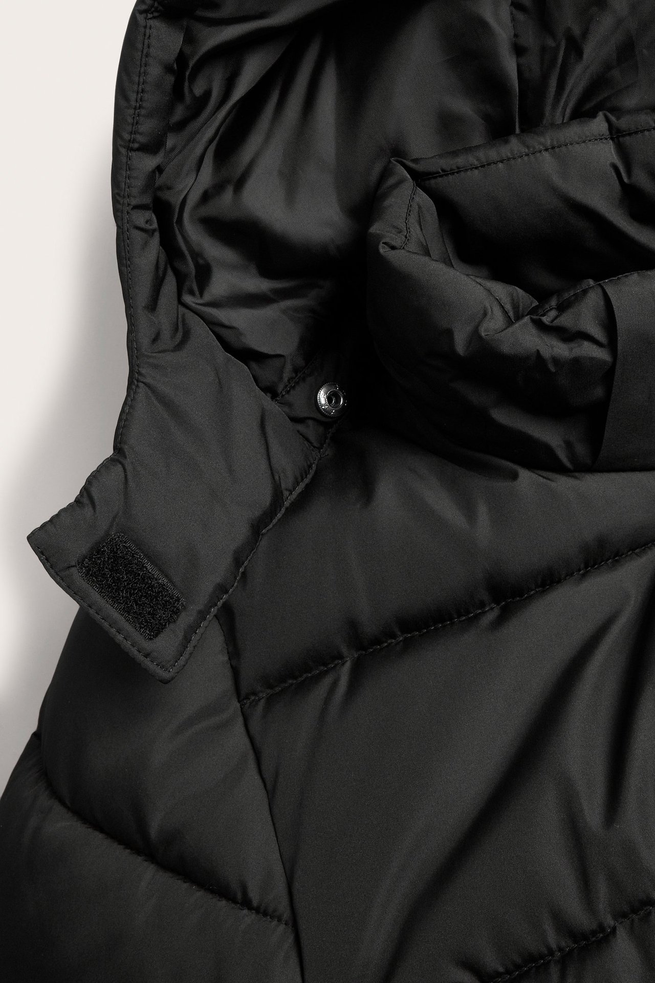 Zbliżenie czarnej pikowanej kurtki puchowej z kapturem, pokazujące zatrzask i zapięcie na rzep.