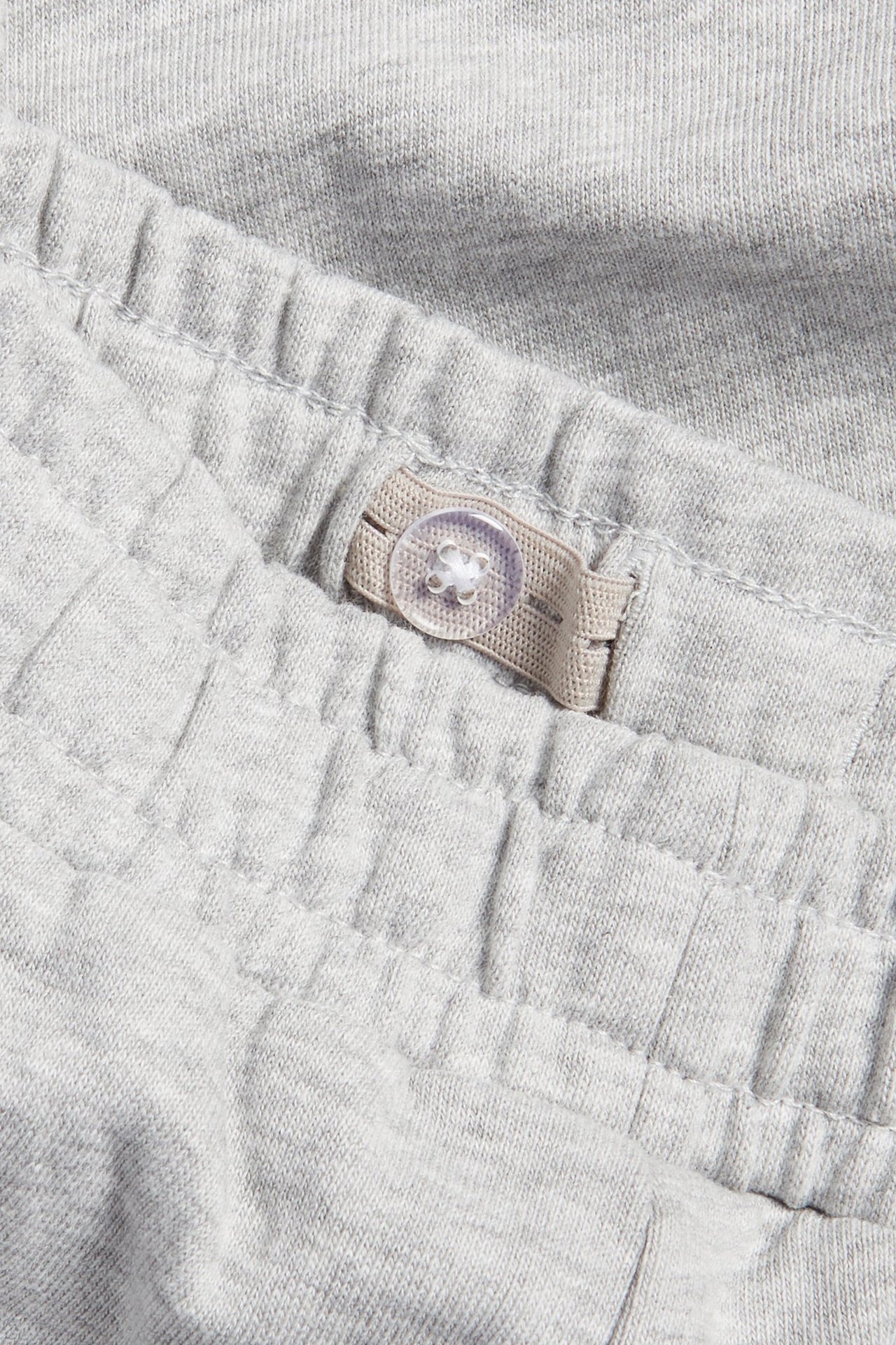 Zbliżenie szarych melanżowych spodni dresowych, pokazujące regulowany elastyczny pas z guzikiem.