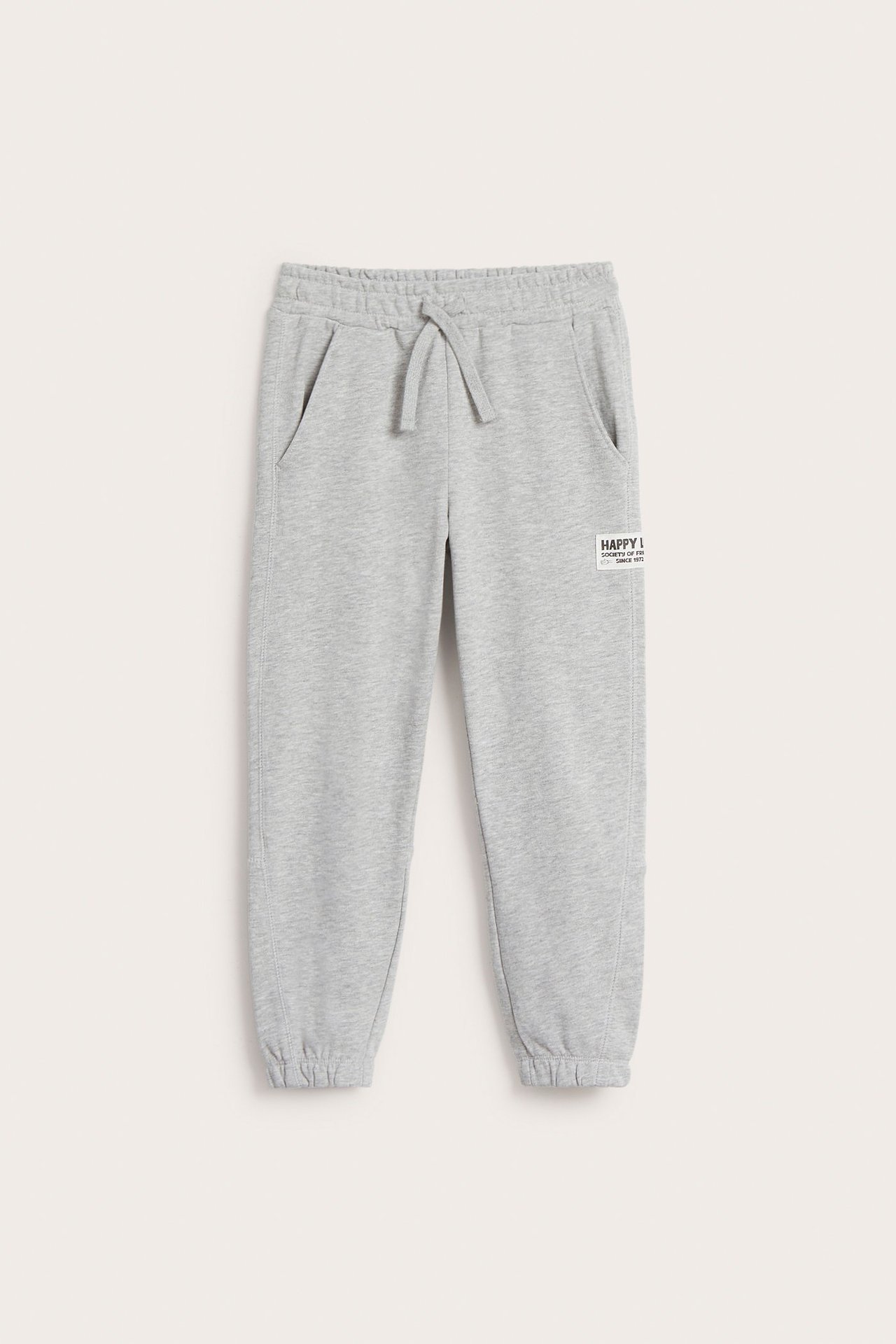 Widok z przodu dziecięcych szarych melanżowych spodni dresowych z elastyczną talią, sznurkiem, kieszeniami i naszywką.