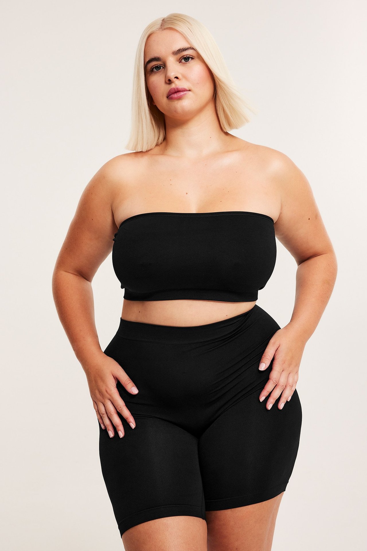 Forfra, kvinne i svarte sømløse shorts og matchende svart bandeau-topp.
