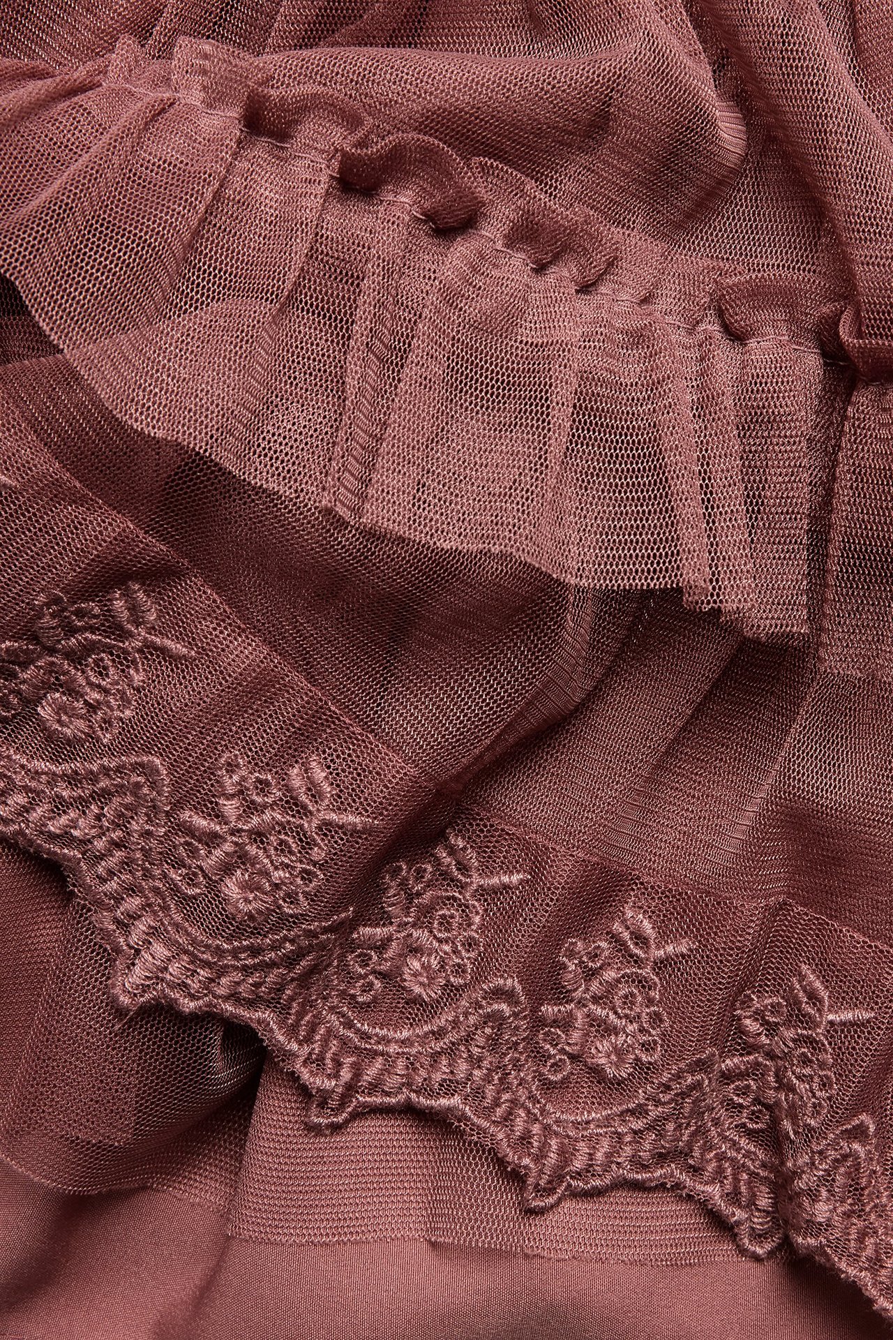 Närbild av en mörkrosa meshkjol med broderade spetsvolanger och polyesterfoder.