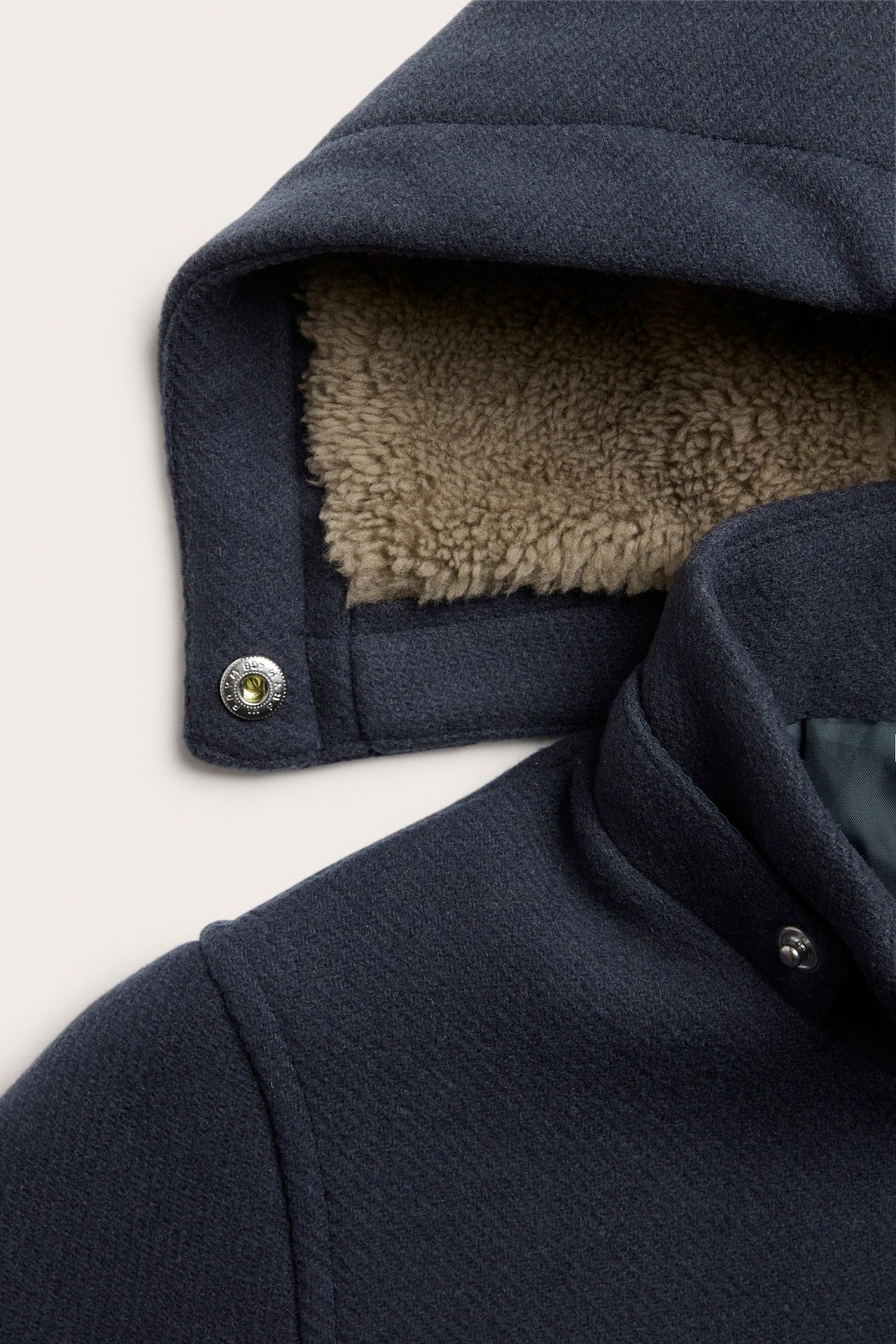 Zbliżenie na granatowy płaszcz z mieszanki wełny z odpinanym kapturem i jasnobrązową podszewką z misia.
