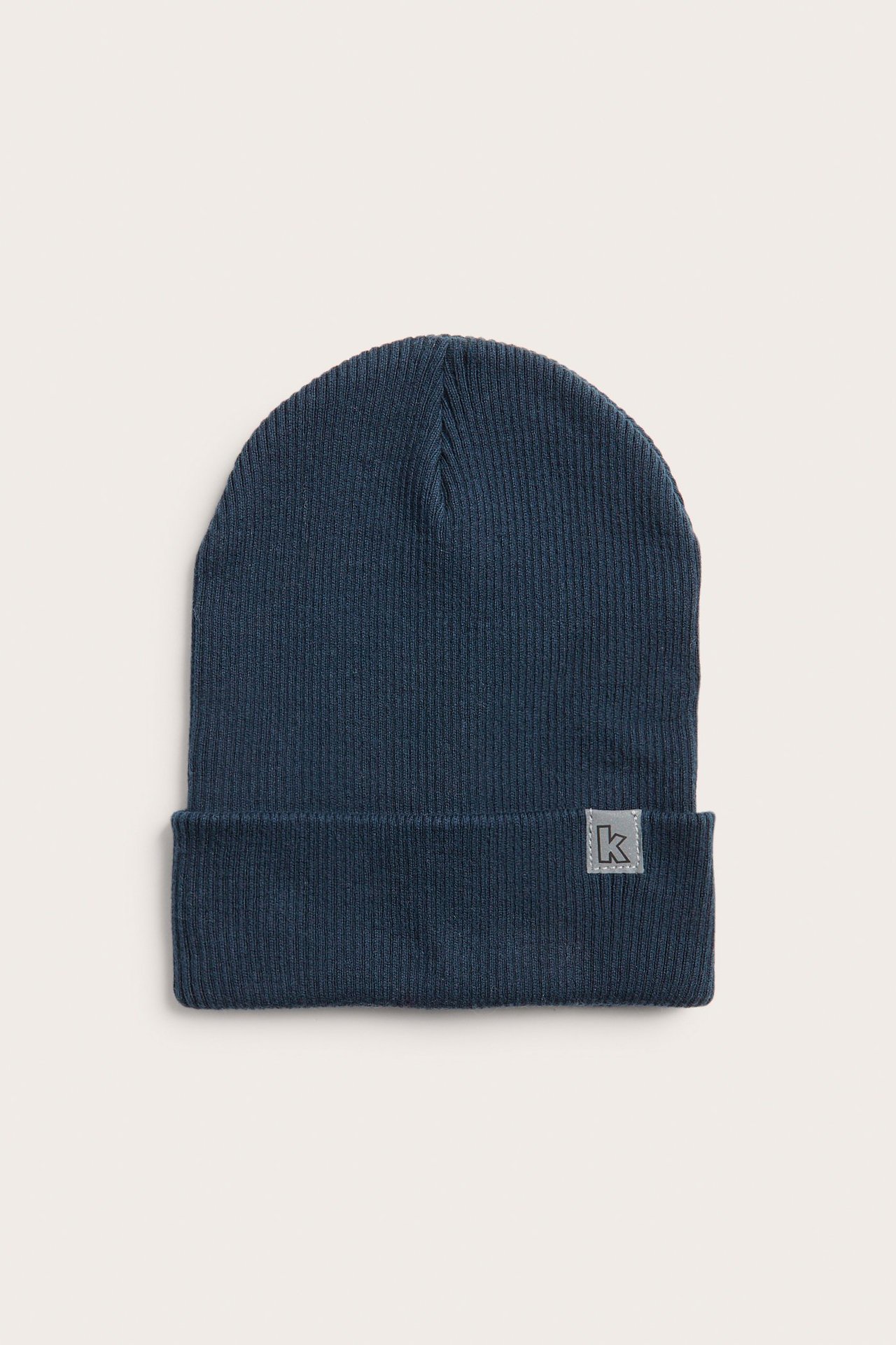 Frontvy av en mörkblå ribbstickad bomullsmössa med uppvikt kant och en liten grå 'k'-etikett.