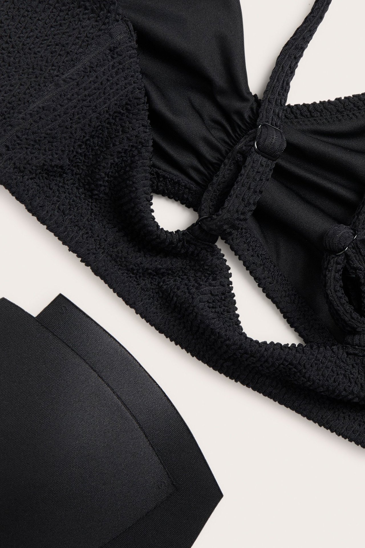 Zbliżenie czarnego teksturowanego biustonosza bikini z marszczeniem z przodu, regulowanymi ramiączkami i dwoma wyjmowanymi czarnymi wkładkami.