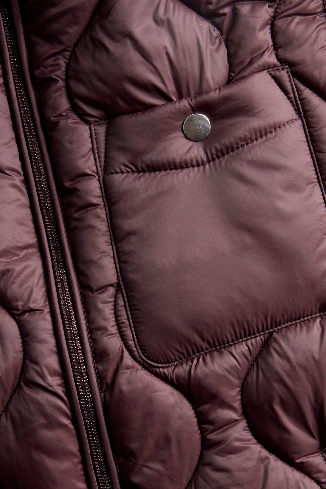 Zbliżenie na bordową pikowaną kamizelkę z zamkiem błyskawicznym i kieszenią na zatrzask.