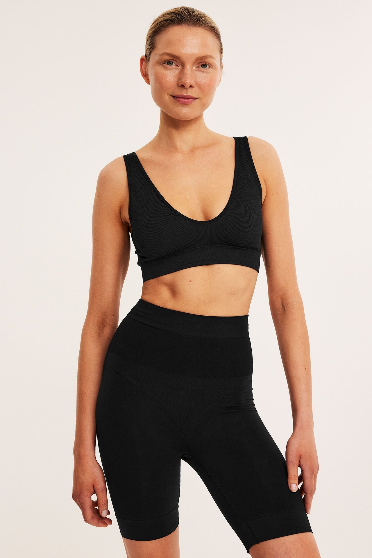 Forfra, kvinne i svarte sømløse high-waist shapingshorts og matchende ribbet BH-topp.