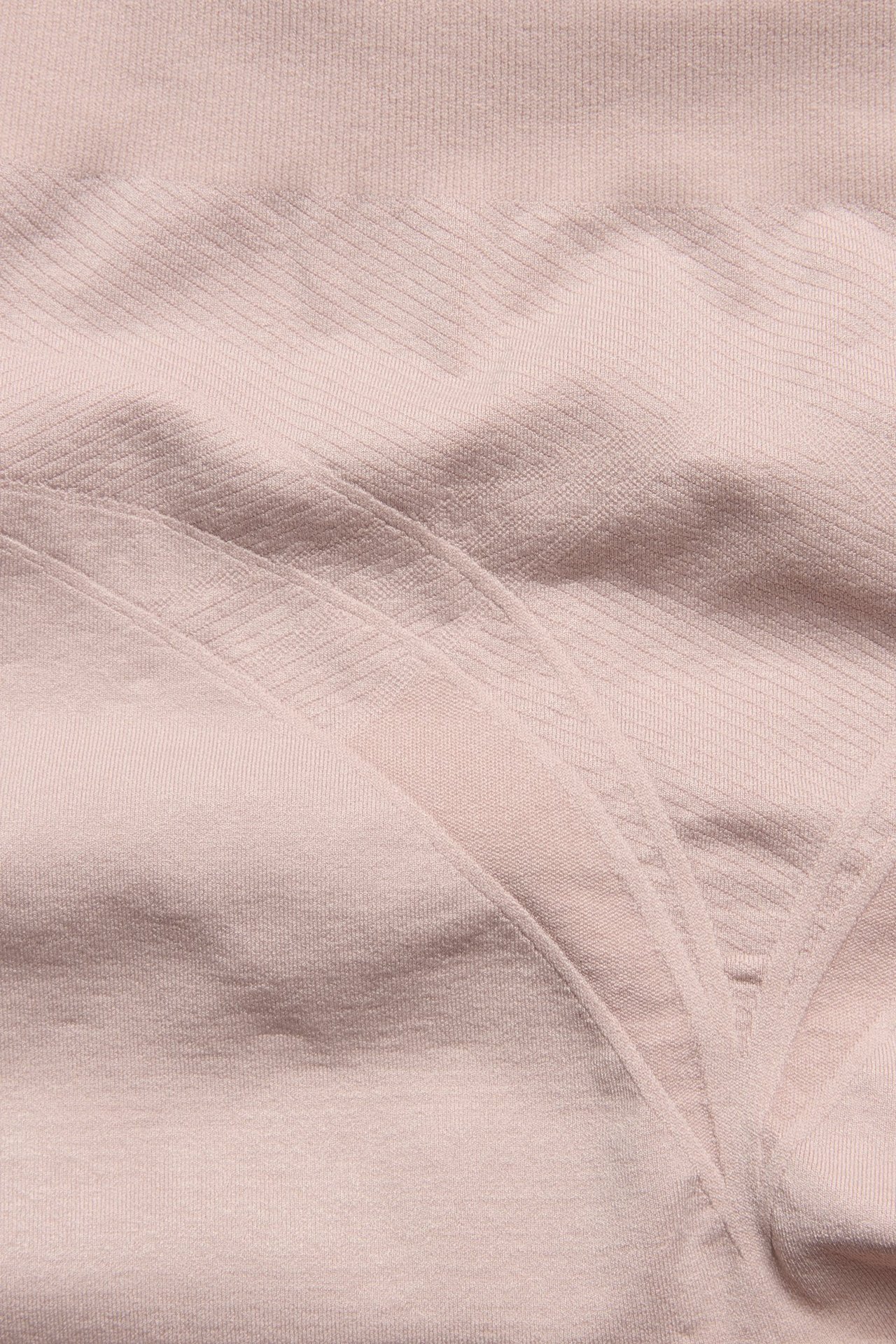 Zbliżenie jasnoróżowych bezszwowych szortów modelujących z subtelnymi prążkowanymi i ukośnymi teksturami.