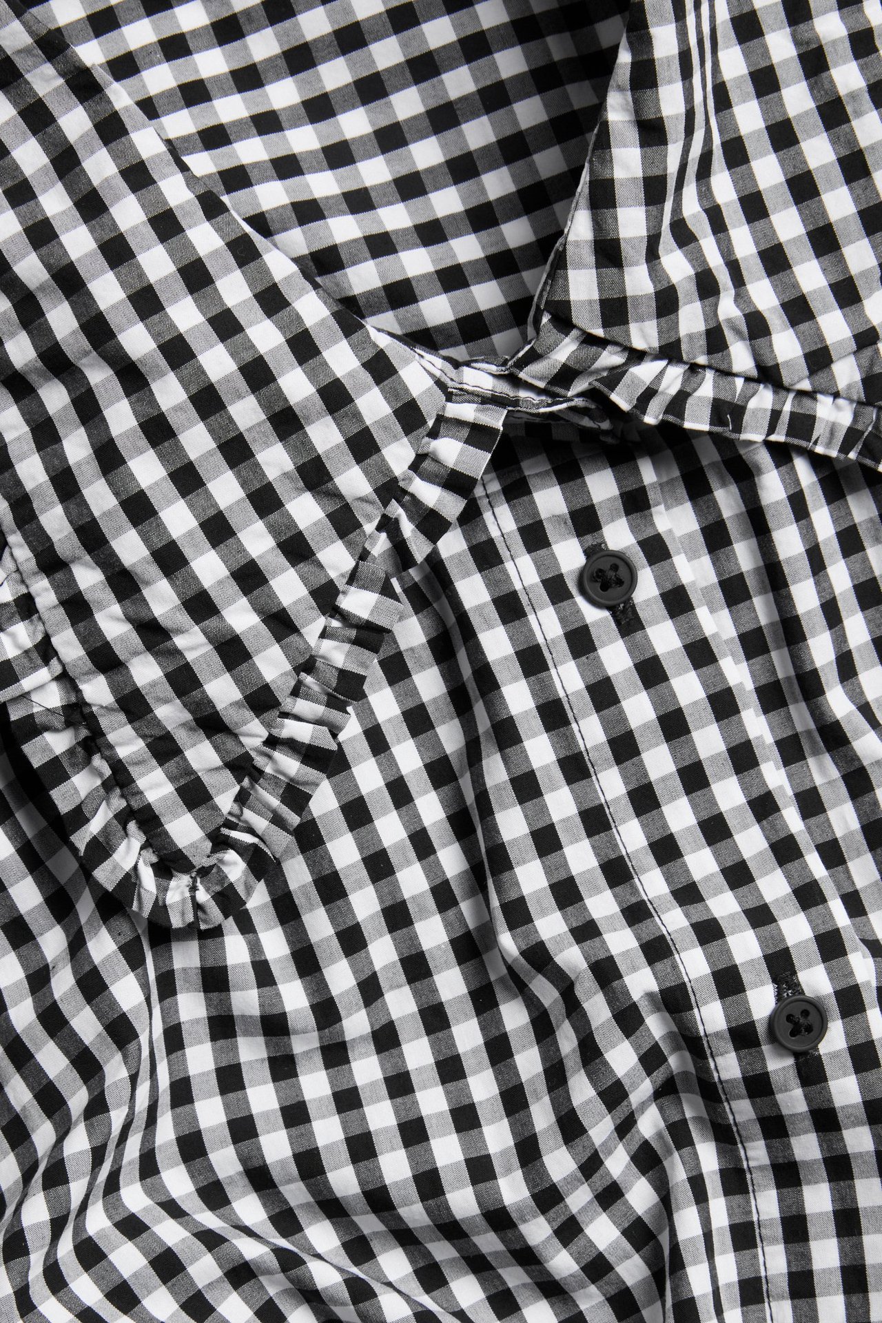 Zbliżenie czarno-białej bawełnianej koszuli w kratkę gingham z falbankowym kołnierzem i zapięciem na guziki.