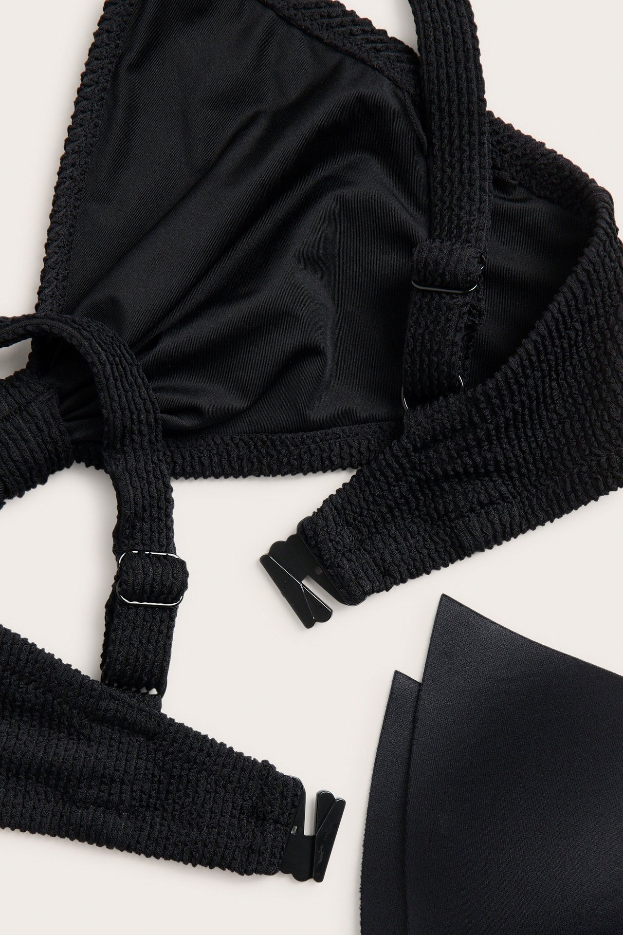 Zbliżenie, leżące płasko, czarnego teksturowanego biustonosza bikini z regulowanymi ramiączkami, zapięciem z tyłu i wyjmowanymi wkładkami.