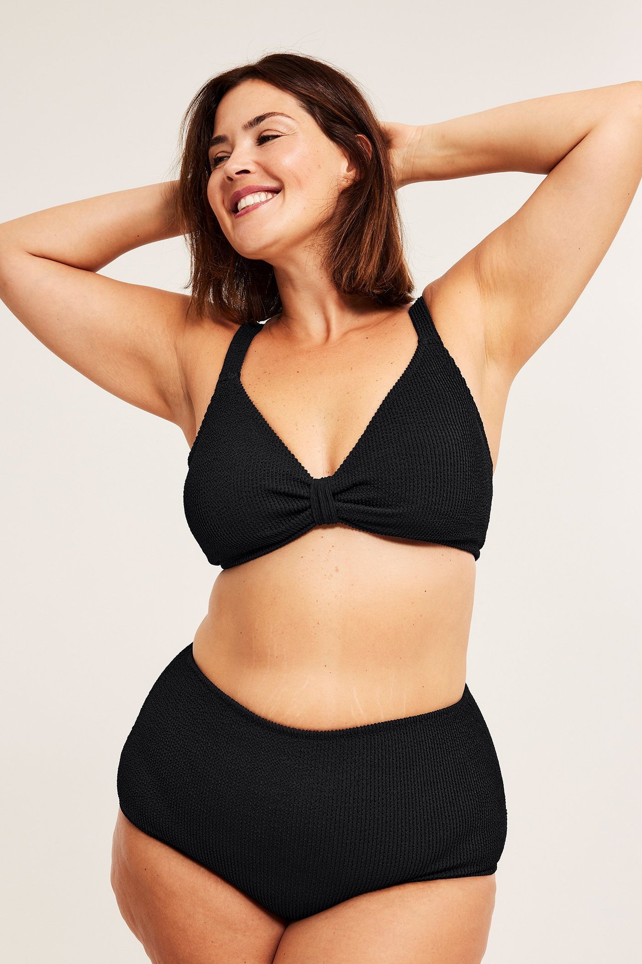 Widok z przodu: kobieta w czarnym, teksturowanym biustonoszu bikini z regulowanymi ramiączkami i pasującymi figami z wysokim stanem.