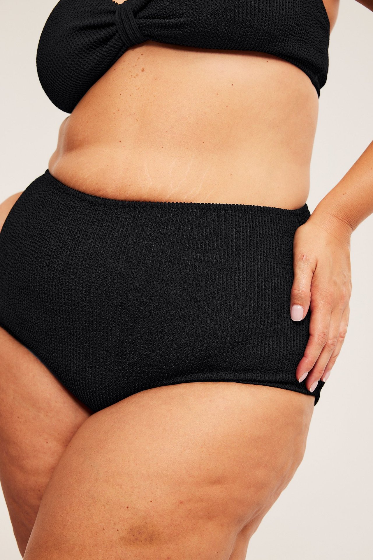 Naisen sivukuva mustissa, korkeavyötäröisissä, kuvioiduissa bikinialaosissa ja yhteensopivassa mustassa bikinitopissa.