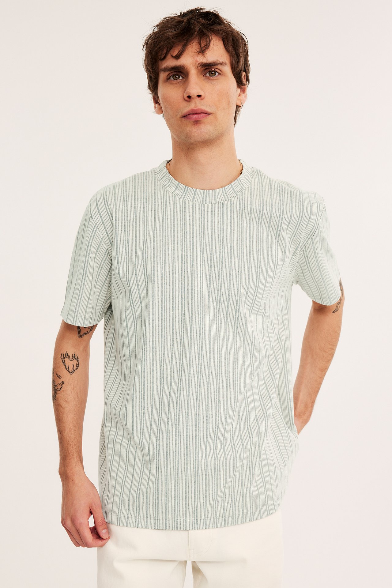 Edestä kuvattu mies yllään vaalea mintunvihreä strukturoitu O-kaula-aukko t-paita ja vaaleat kermanväriset housut.