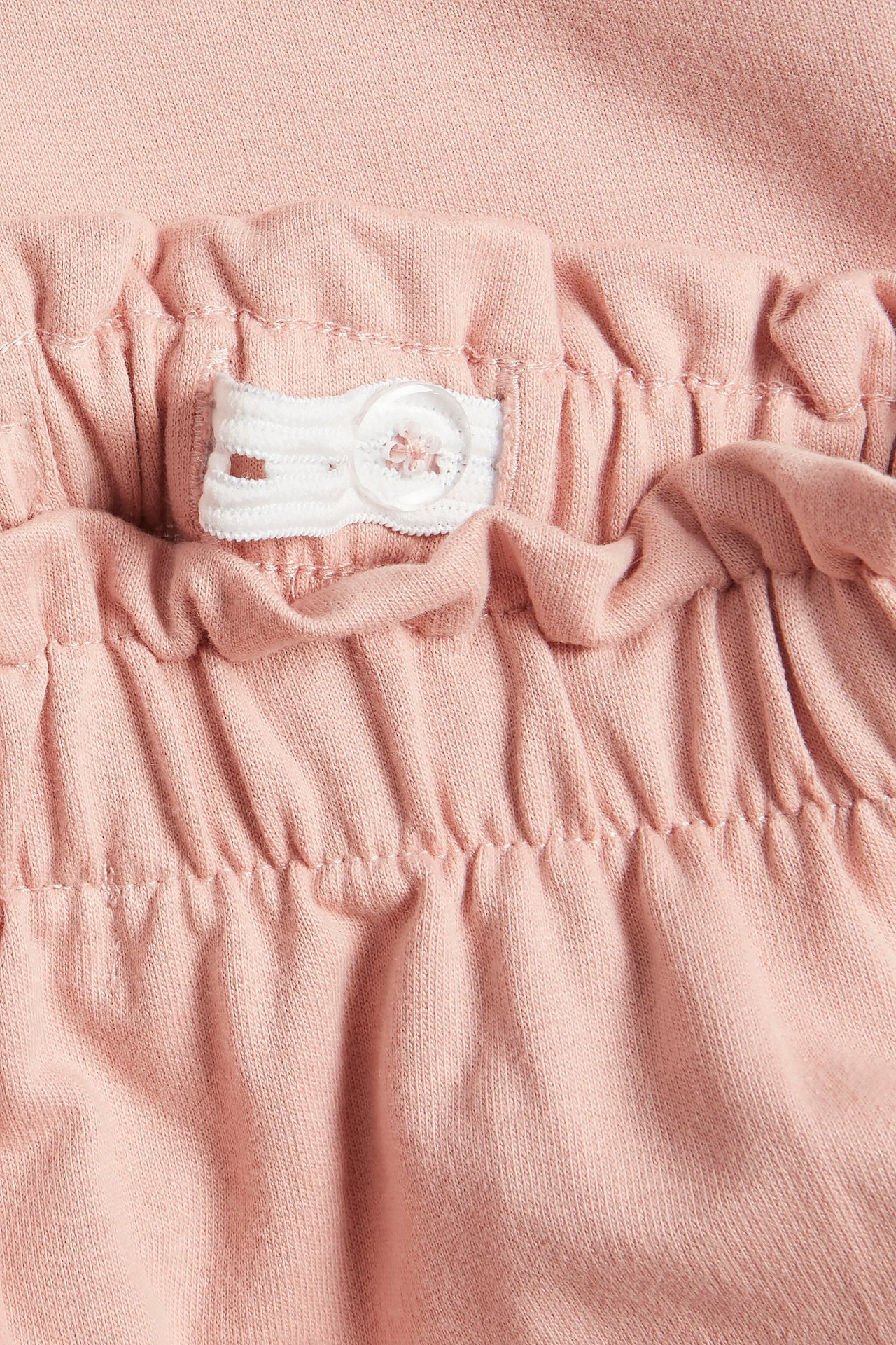 Lähikuva vaaleanpunaisista puuvillaisista collegehousuista, joissa säädettävä kuminauha ja valkoinen nappi.