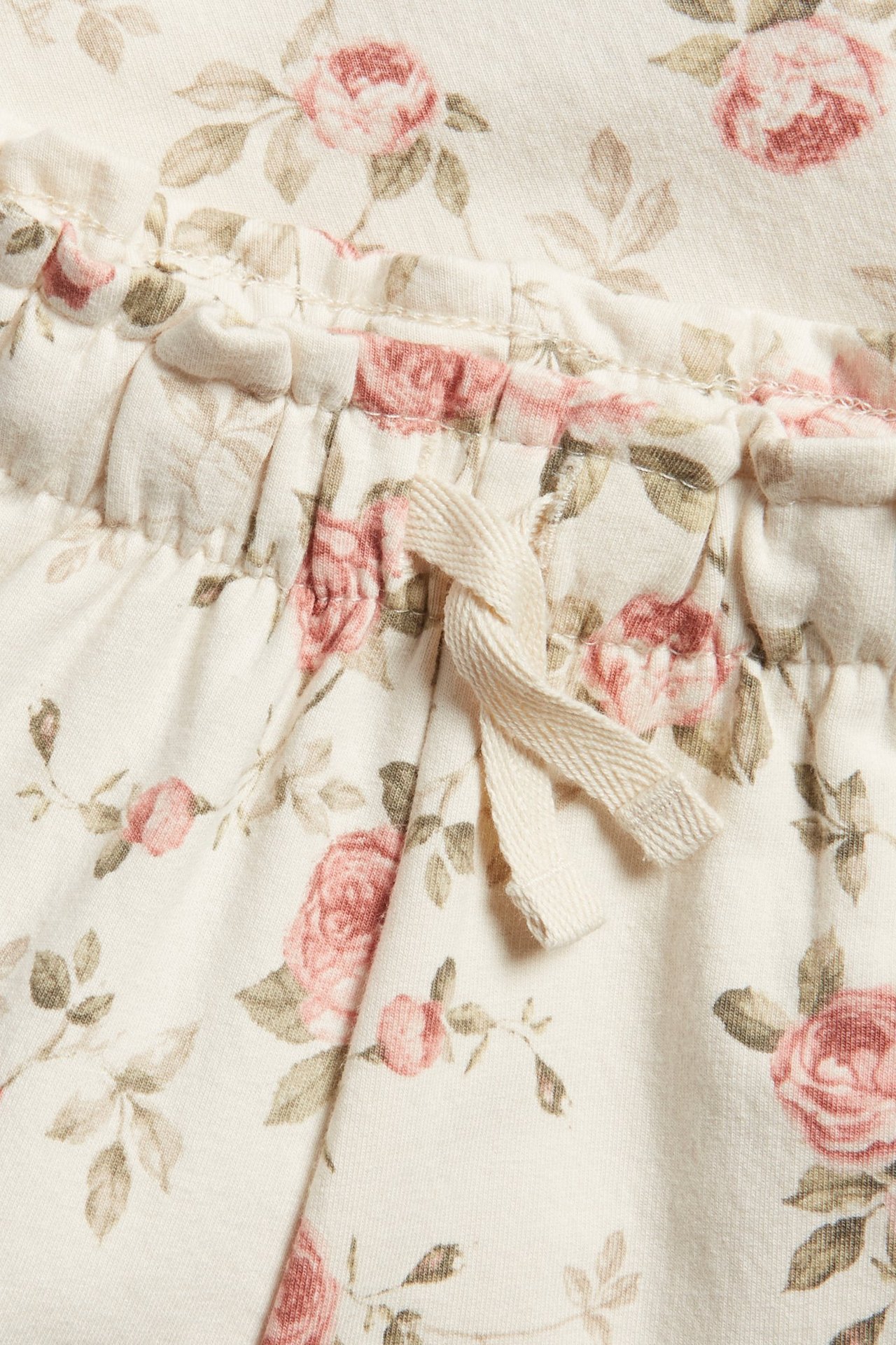 Zbliżenie na jasnobeżowe kwieciste spodnie dresowe z elastyczną talią, falbanką i zawiązanym sznurkiem.