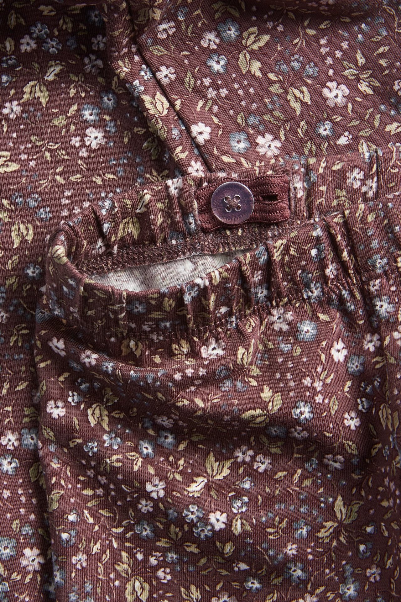 Zbliżenie na ciemnośliwkowe legginsy w kwiaty z regulowaną elastyczną talią i guzikiem.