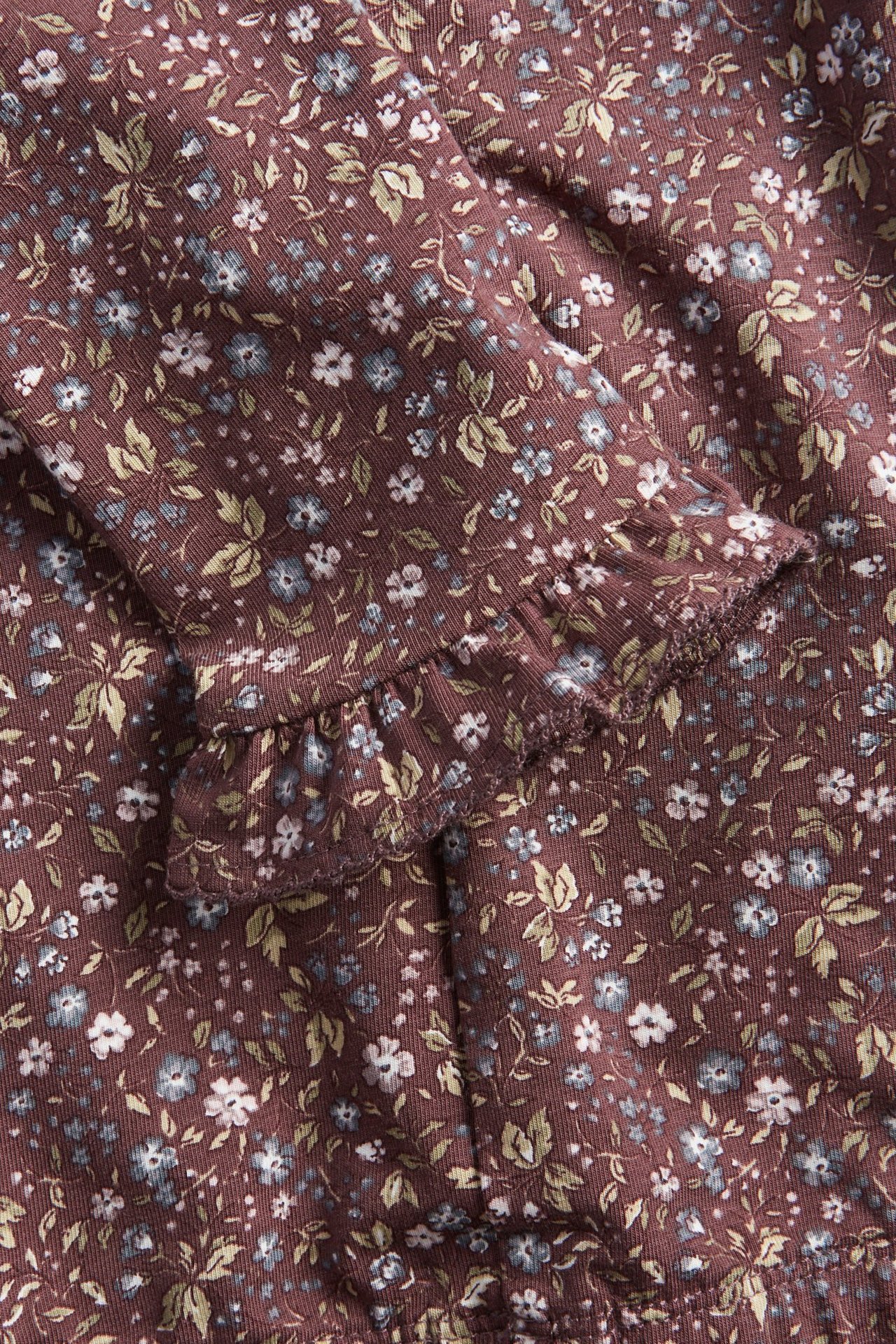 Lähikuva lasten tumman luumunvärisistä kukkakuvioisista leggingseistä, joissa on röyhelö nilkassa.