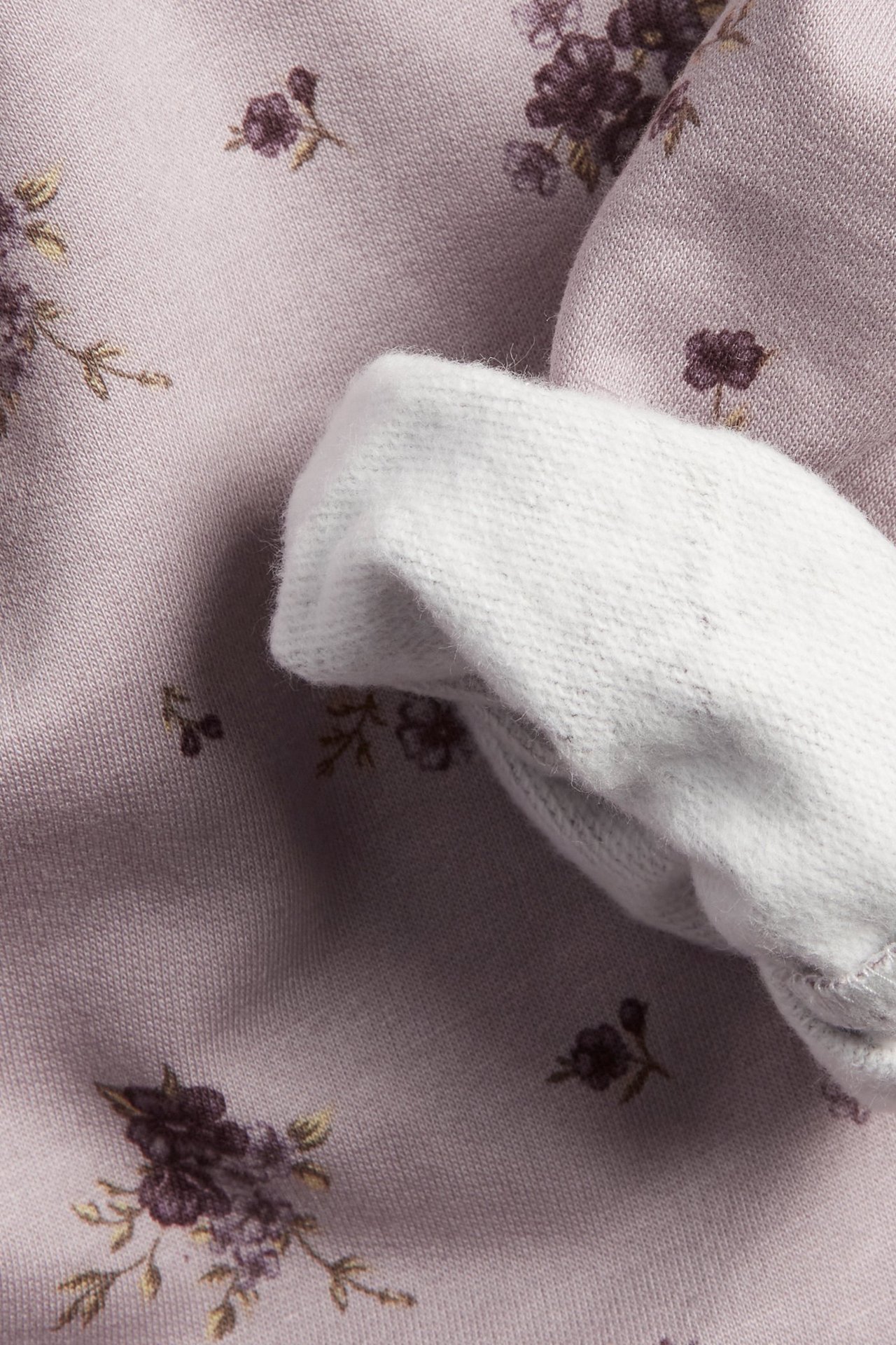 Lähikuva vaaleanliilasta kukkakuosisesta puuvillapaidasta, jossa valkoinen ribattu hihansuu.