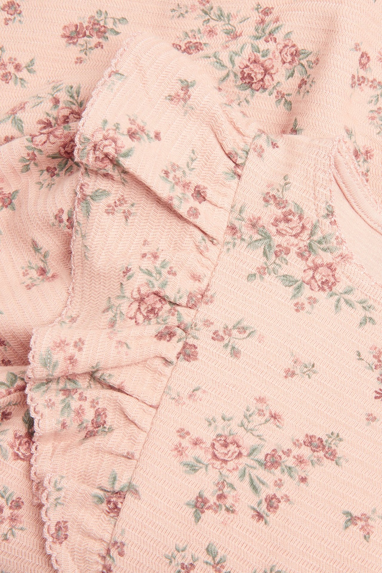 Zbliżenie różowej sukienki w kwiaty z teksturowanej dzianiny z falbankami.