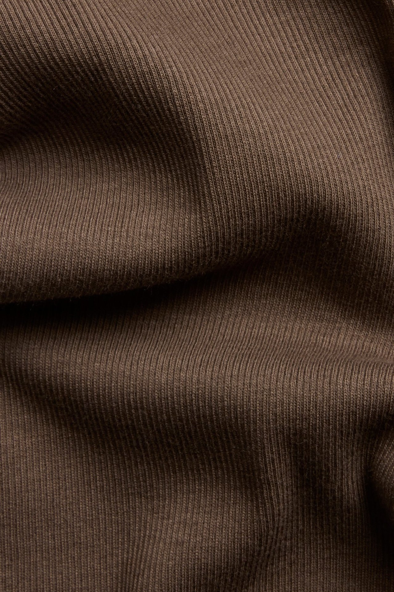 Zbliżenie na ciemnobrązowy prążkowany materiał legginsów z widoczną pionową teksturą.