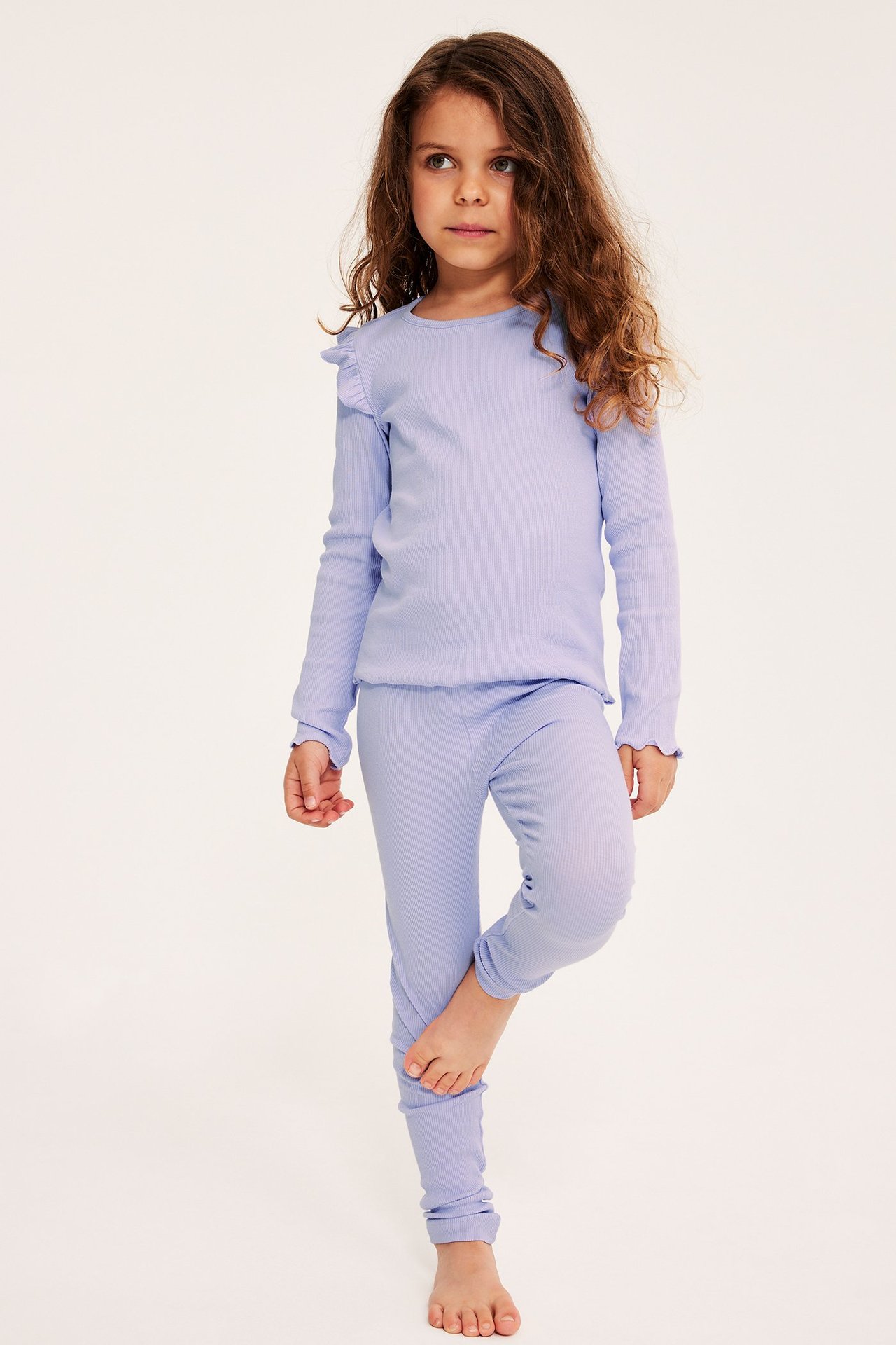 Edestäpäin: lapsi yllään vaaleanliilat ribbileggingsit ja yhteensopiva pitkähihainen toppi röyhelöillä.
