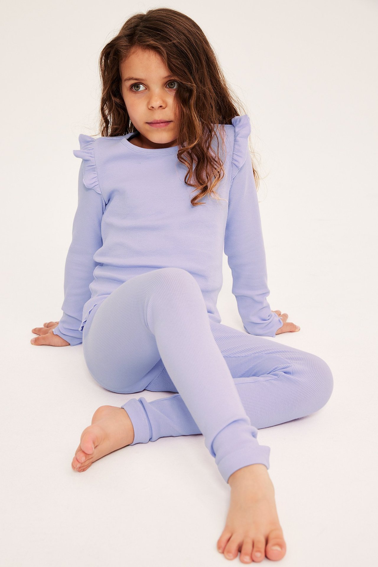 Edestä, lapsi yllään vaaleanliilat ribatut leggingsit ja yhteensopiva pitkähihainen toppi olkapäärypyillä.