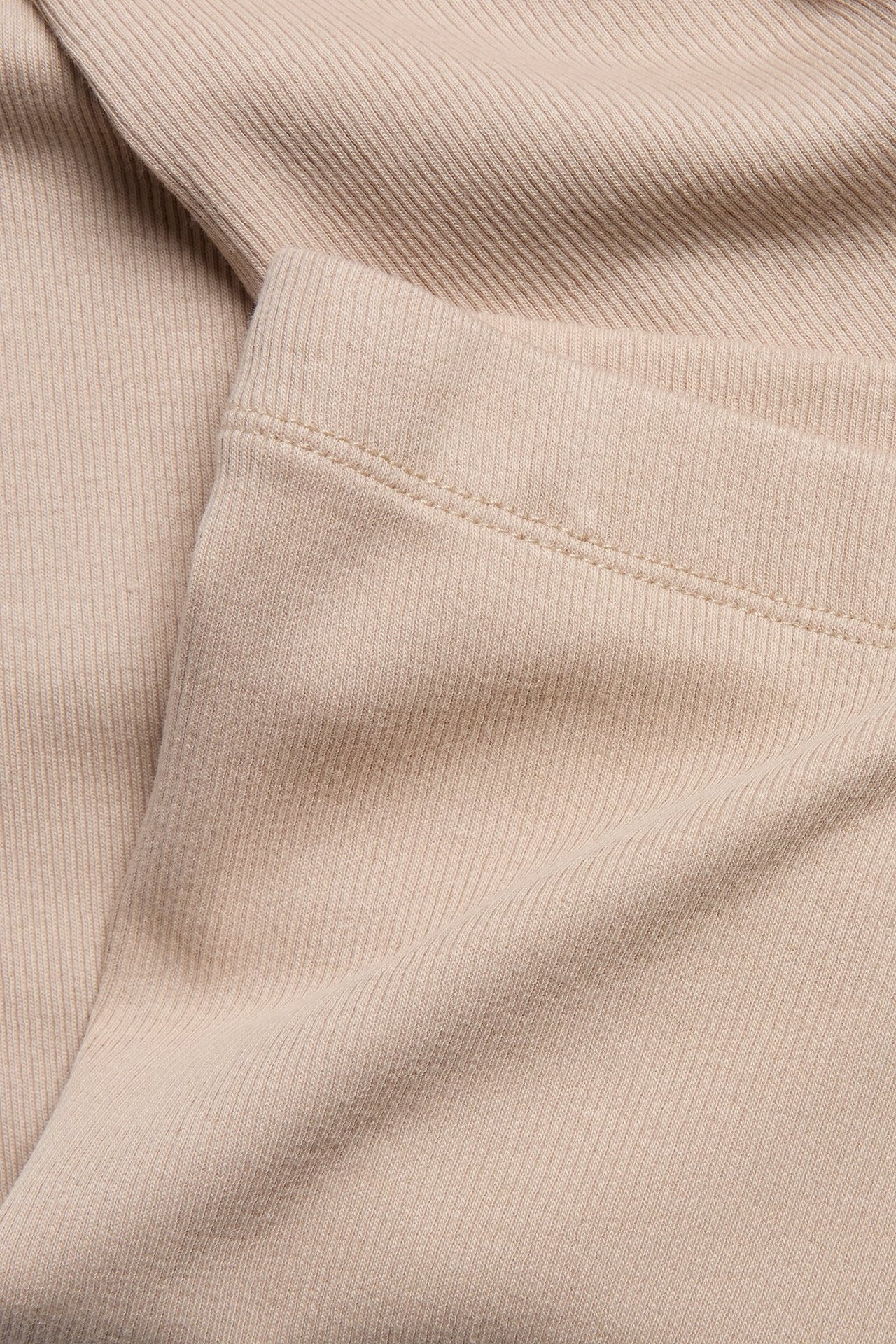 Zbliżenie beżowych legginsów w prążki, ukazujące prążkowaną teksturę materiału.