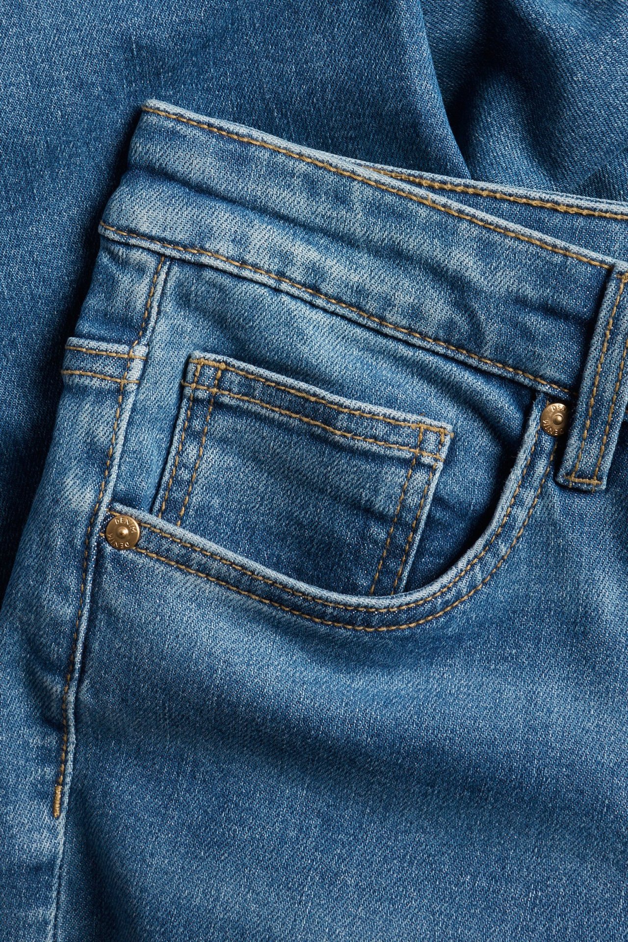 Zbliżenie na niebieskie jeansy straight z denimu z kontrastowymi szwami i przednią kieszenią.