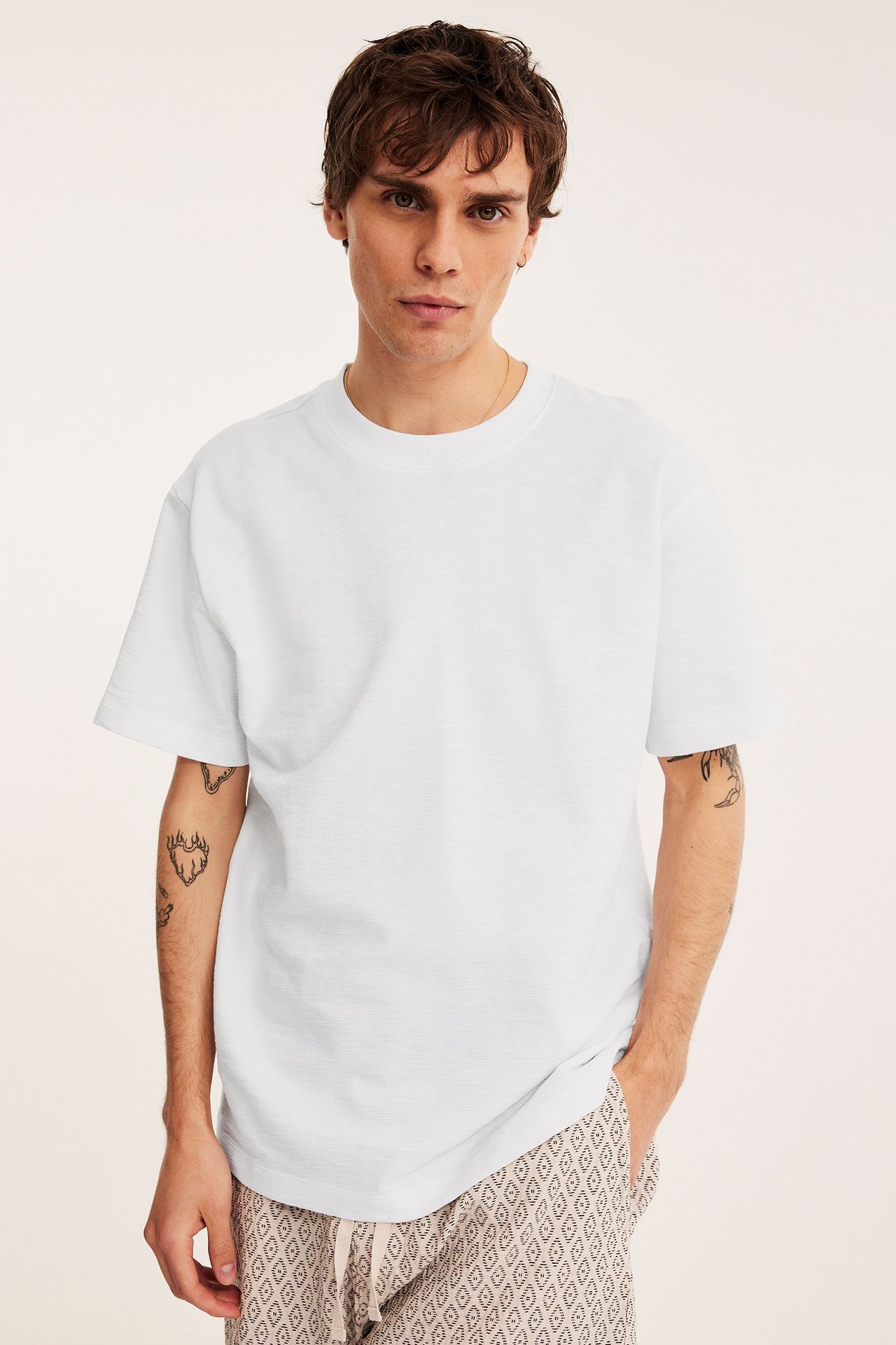 Widok z przodu mężczyzny w białym, luźnym bawełnianym T-shircie i wzorzystych szortach.