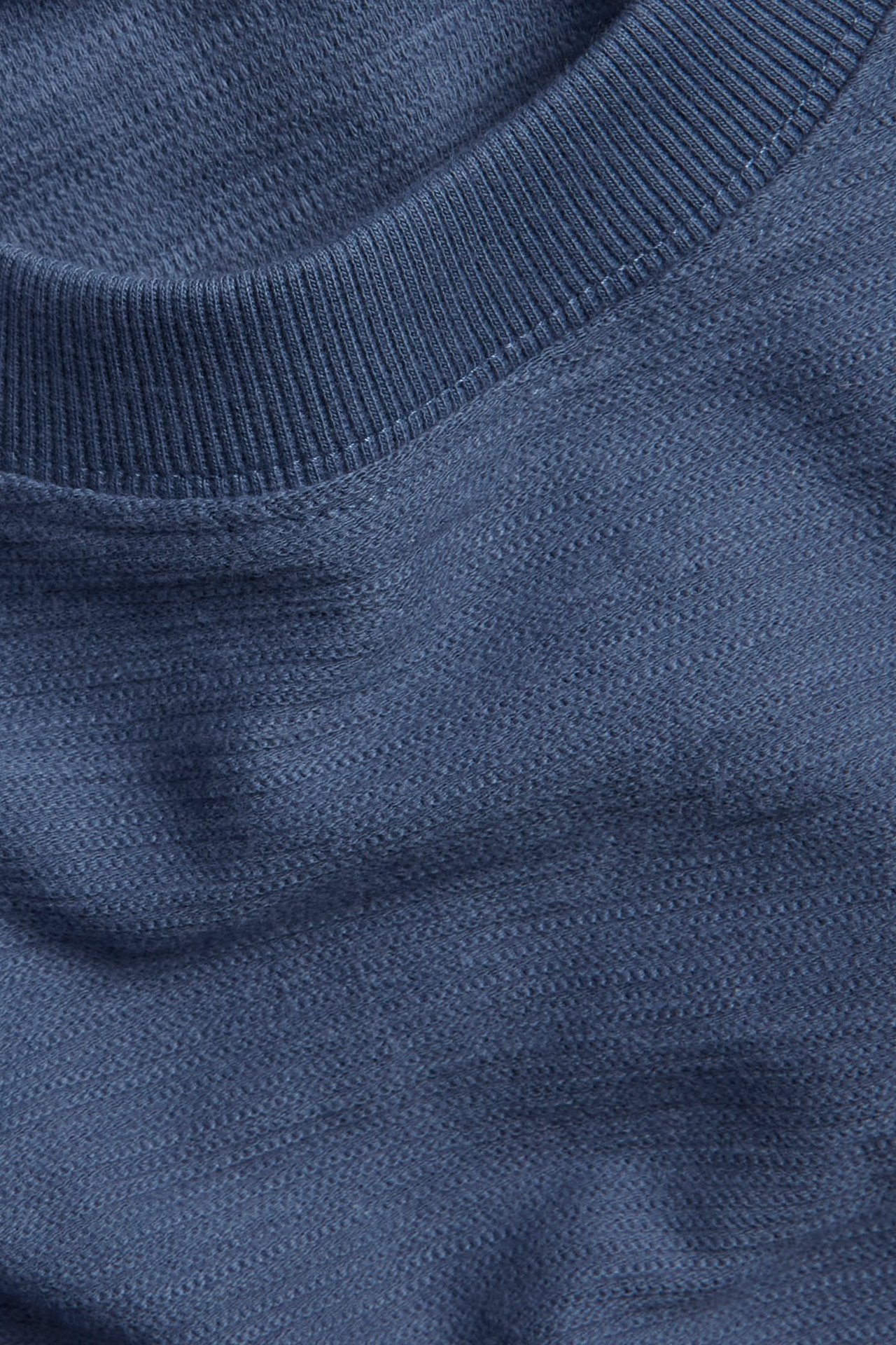 Zbliżenie na niebieski, luźny bawełniany t-shirt z prążkowanym okrągłym dekoltem i teksturowanym materiałem.