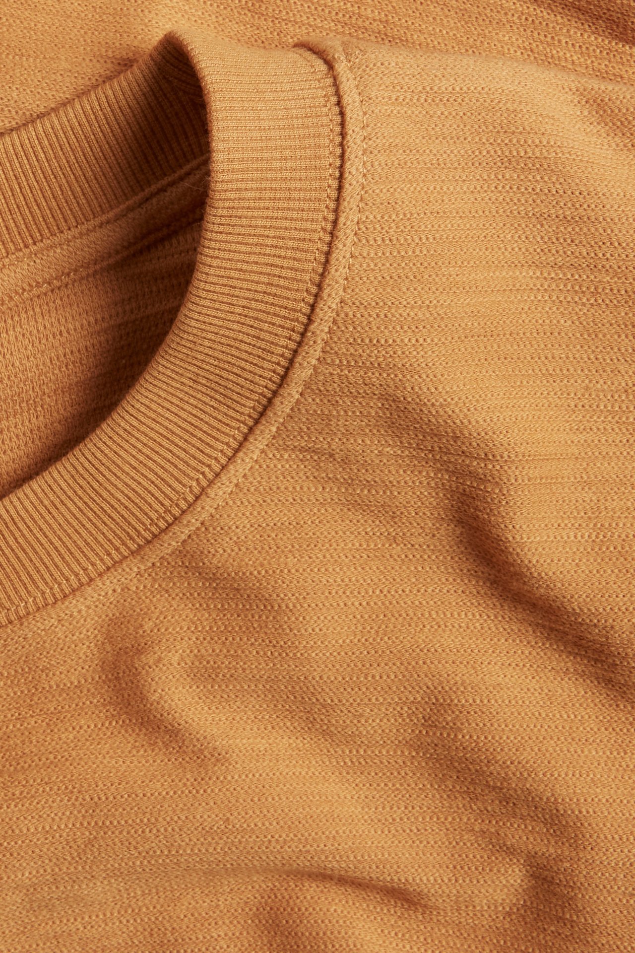 Närbild av en beige lös passform rundhalsad t-shirt i strukturerad bomull med ribbad halsringning.