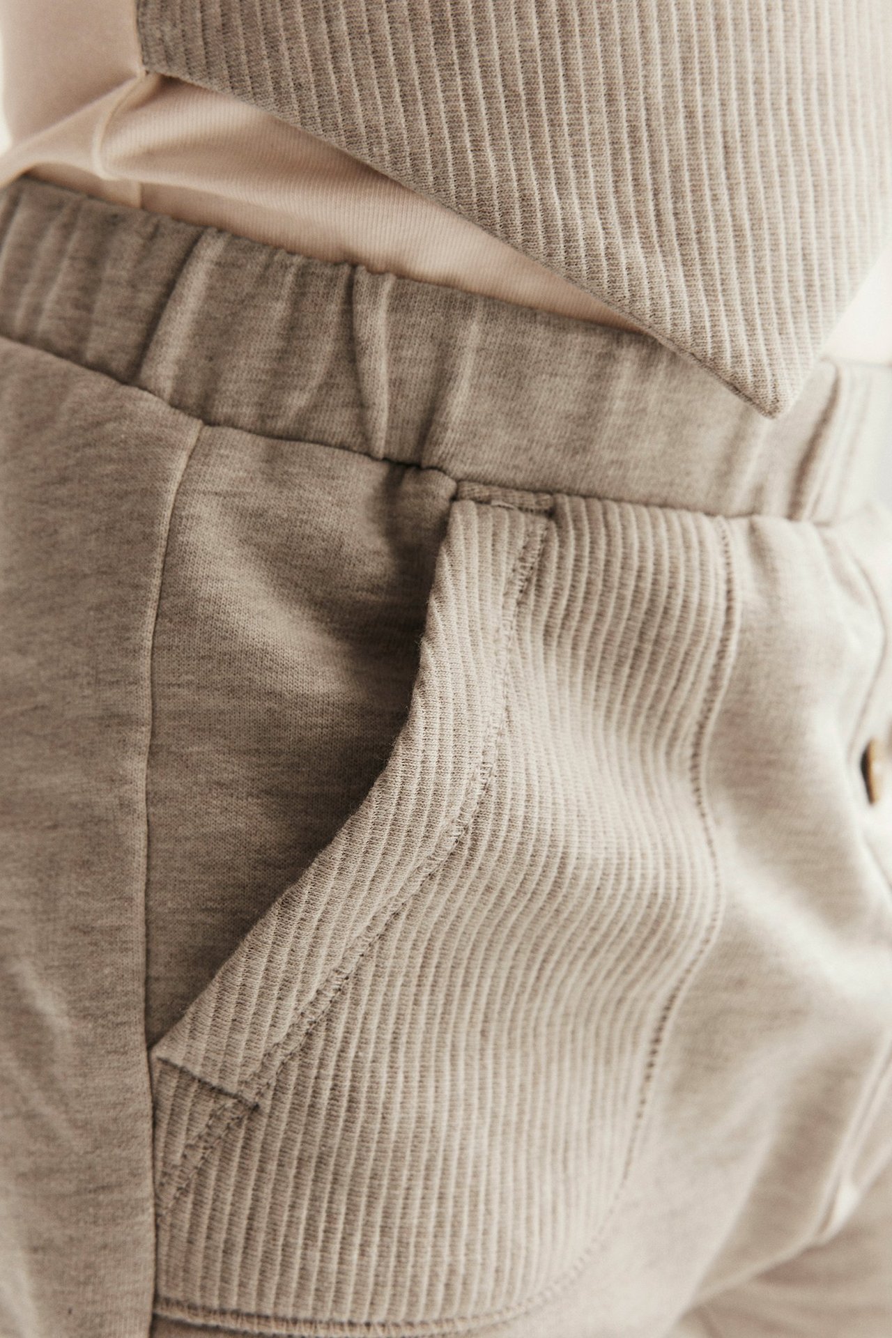 Zbliżenie na beżowo-melanżowe bawełniane spodnie dresowe dla dziecka z prążkowanymi kieszeniami i jasnym topem.