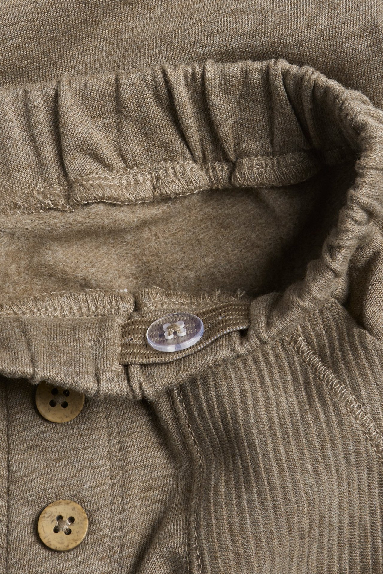 Lähikuva ruskeista meleeratuista puuvillahousuista, joustava vyötärö, säädettävä kuminauha, koristepainikkeet.