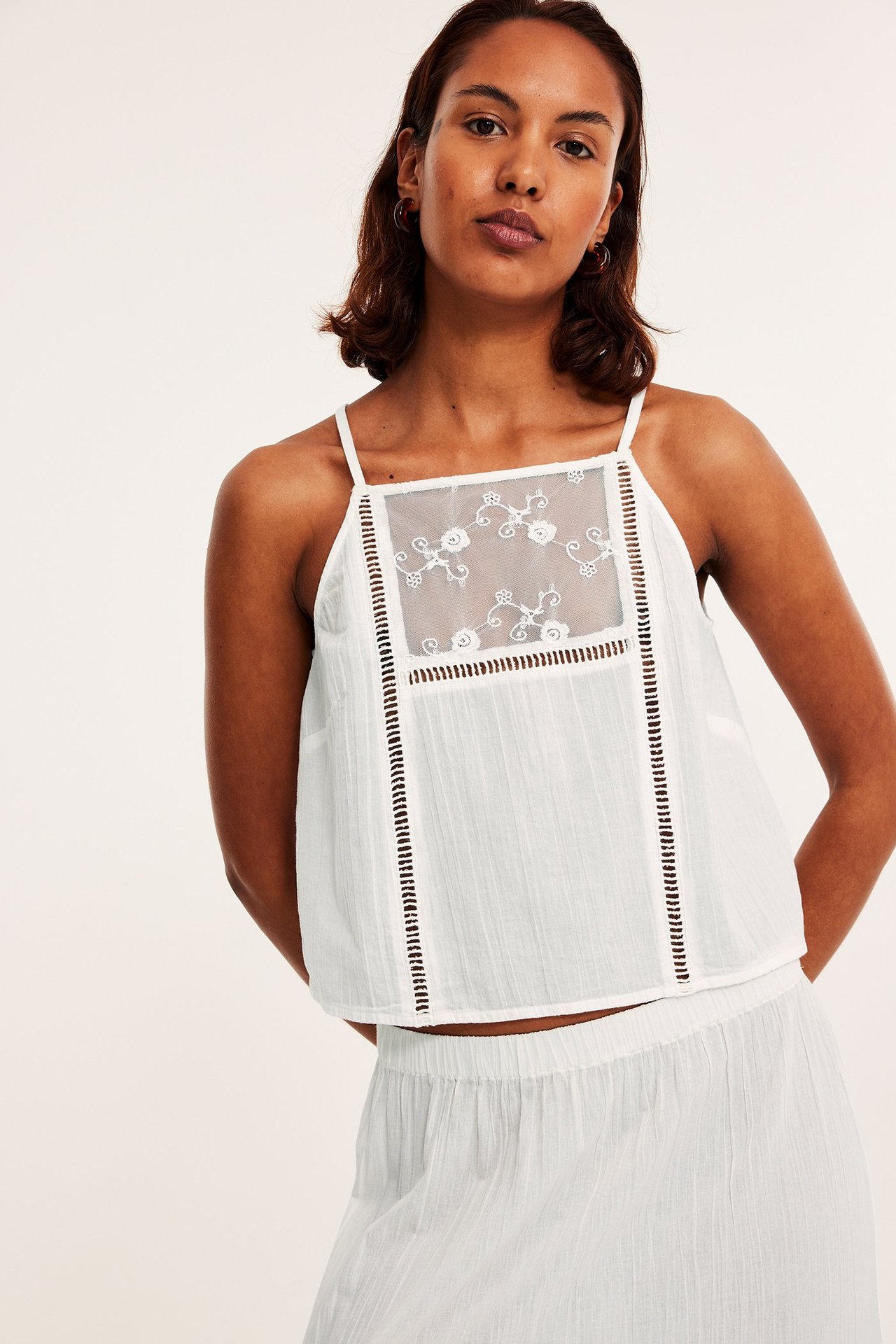 Forfra: kvinne i offwhite camisole med brodert blondeinnfelling og matchende teksturert skjørt.