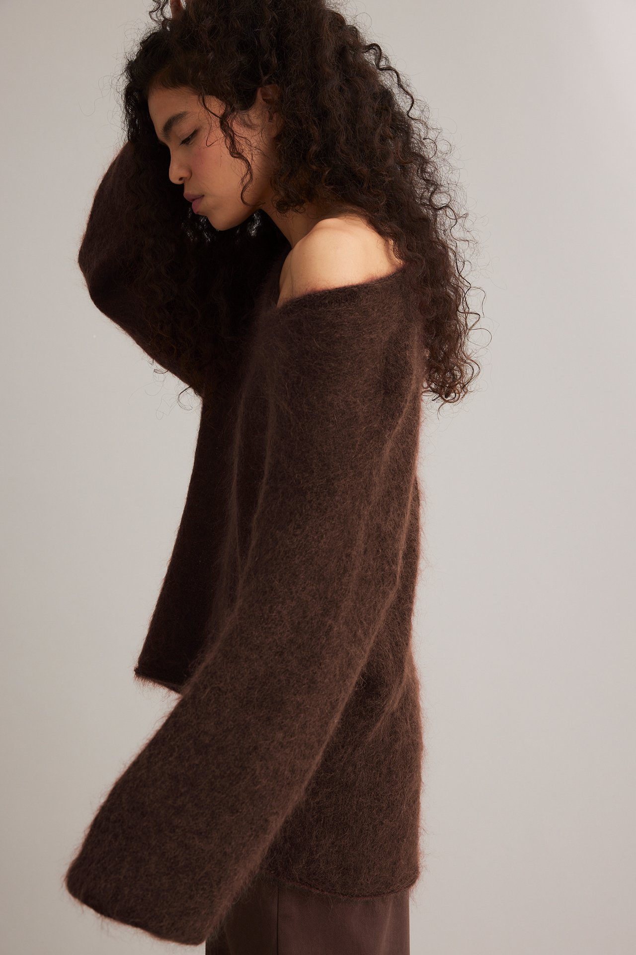 Sidebilde av kvinne i løs, vinrød mohairblanding off-shoulder genser med vide ermer.