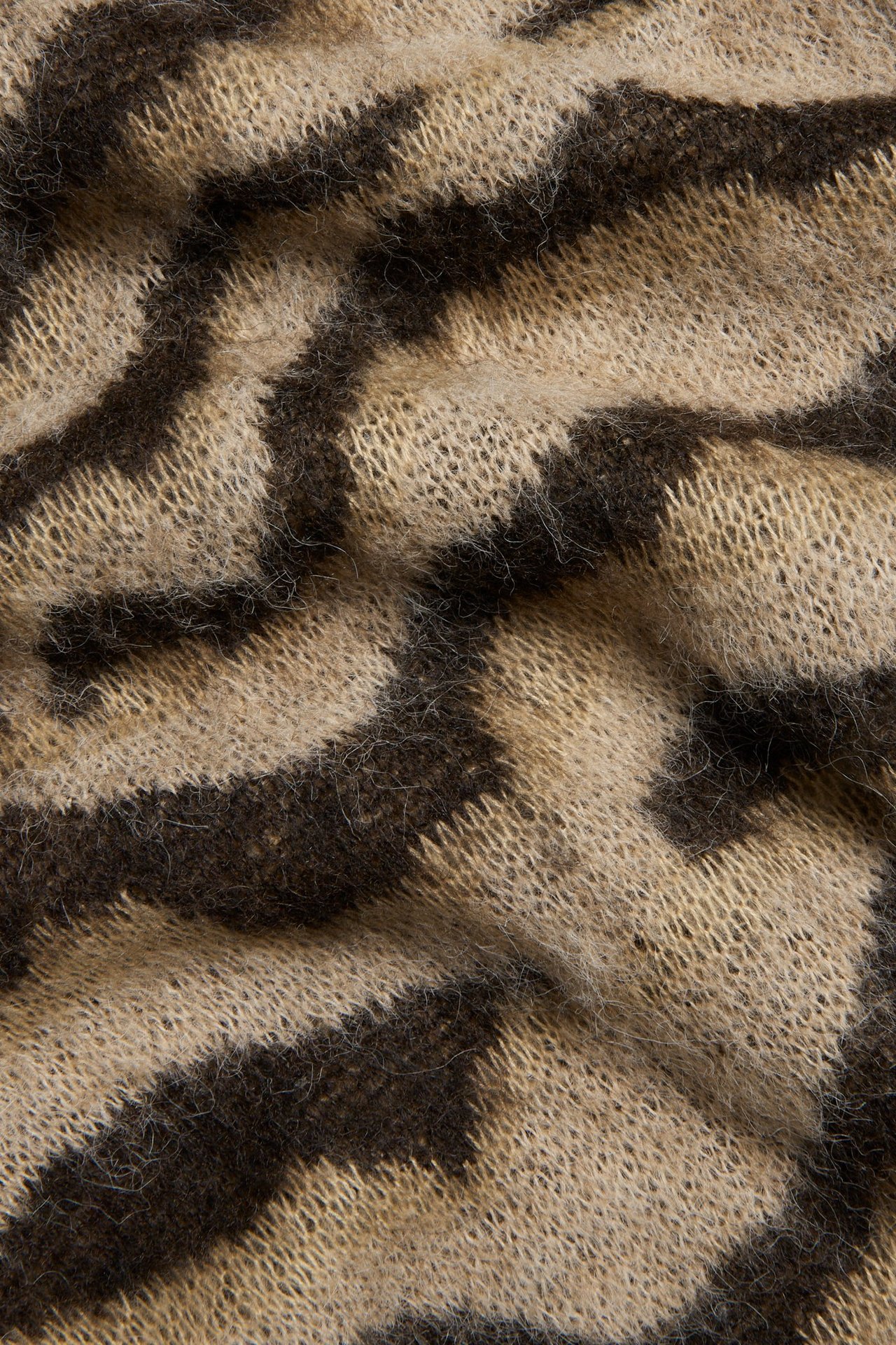 Zbliżenie jasnobeżowej i ciemnobrązowej dzianinowej spódnicy w zebrę z puszystą teksturą.