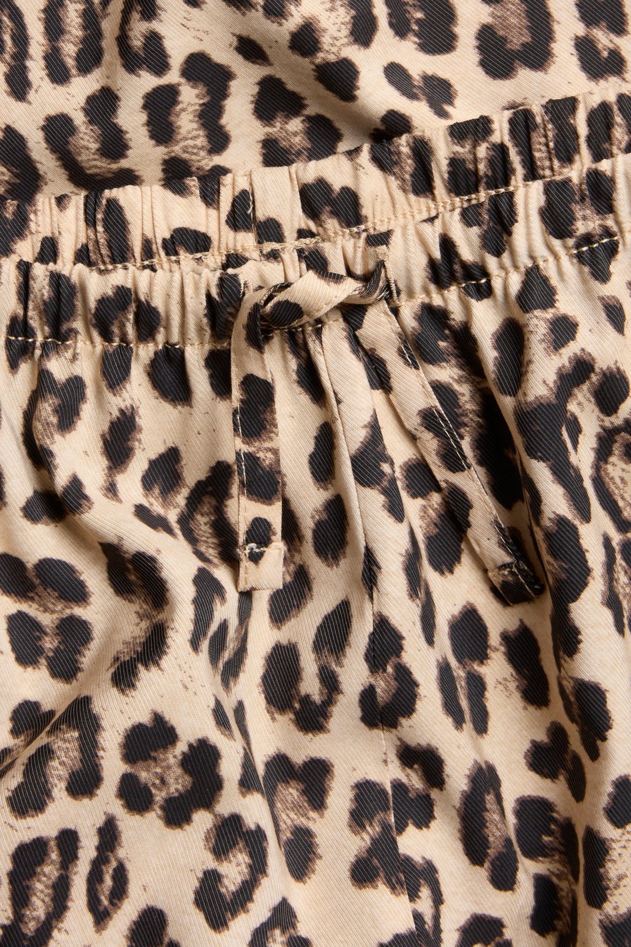 Zbliżenie beżowych i ciemnobrązowych spodni w panterkę z elastycznym pasem ze sznurkiem.
