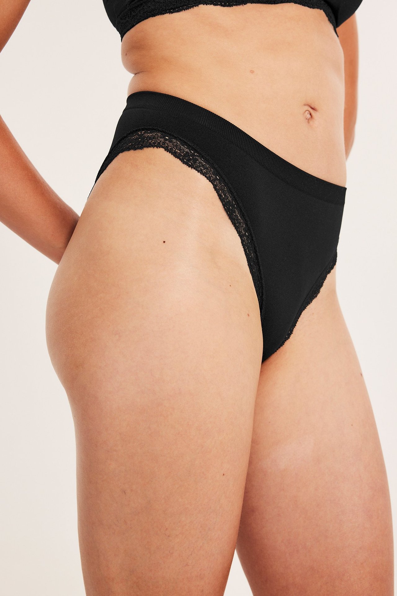 Sidovy av kvinna i svarta sömlösa trosor med spetskant och matchande svart sömlös BH.