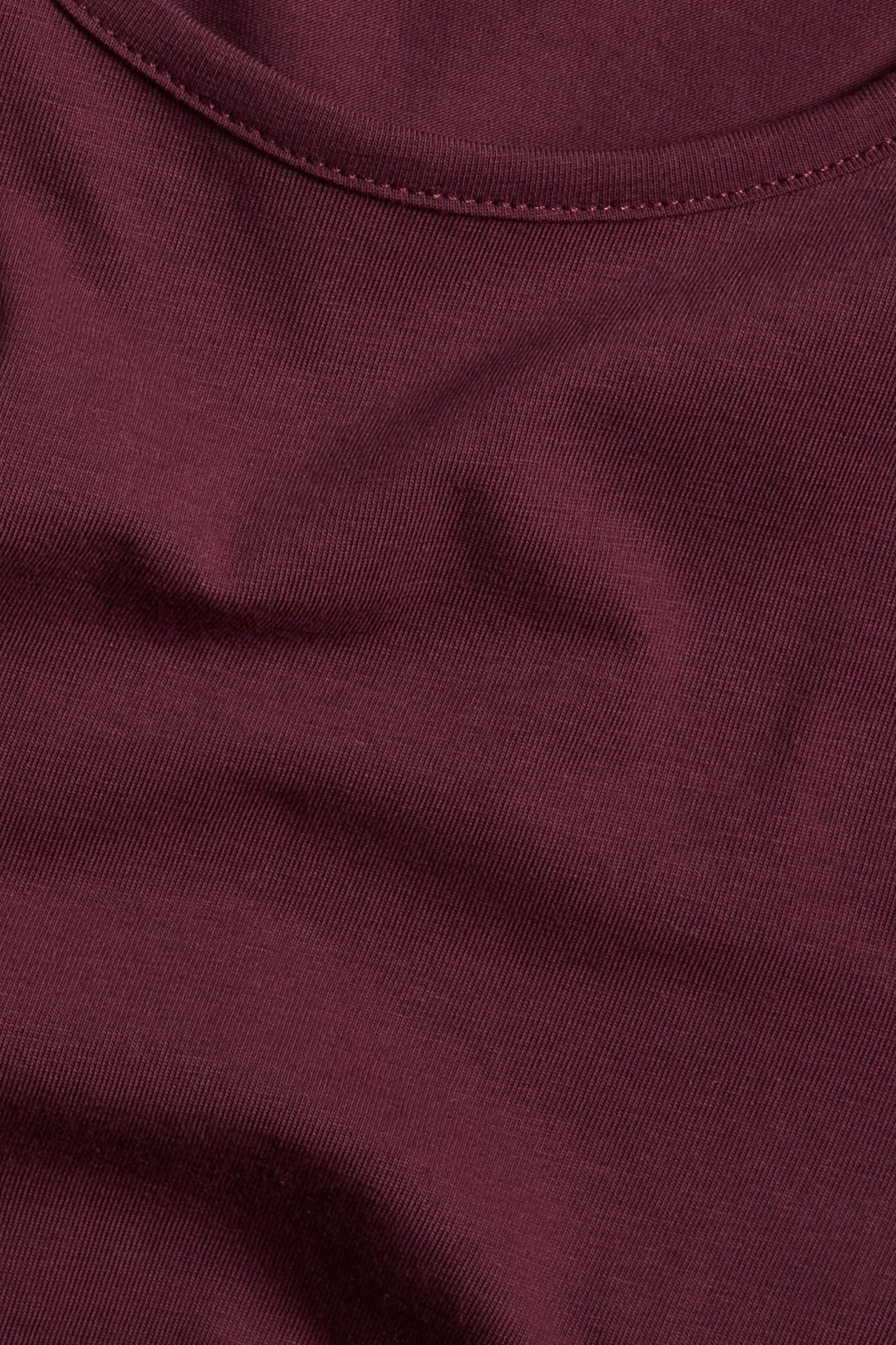 Zbliżenie na ciemnoczerwoną, jednolitą koszulkę z mieszanki bawełny z okrągłym dekoltem i widocznymi szwami.