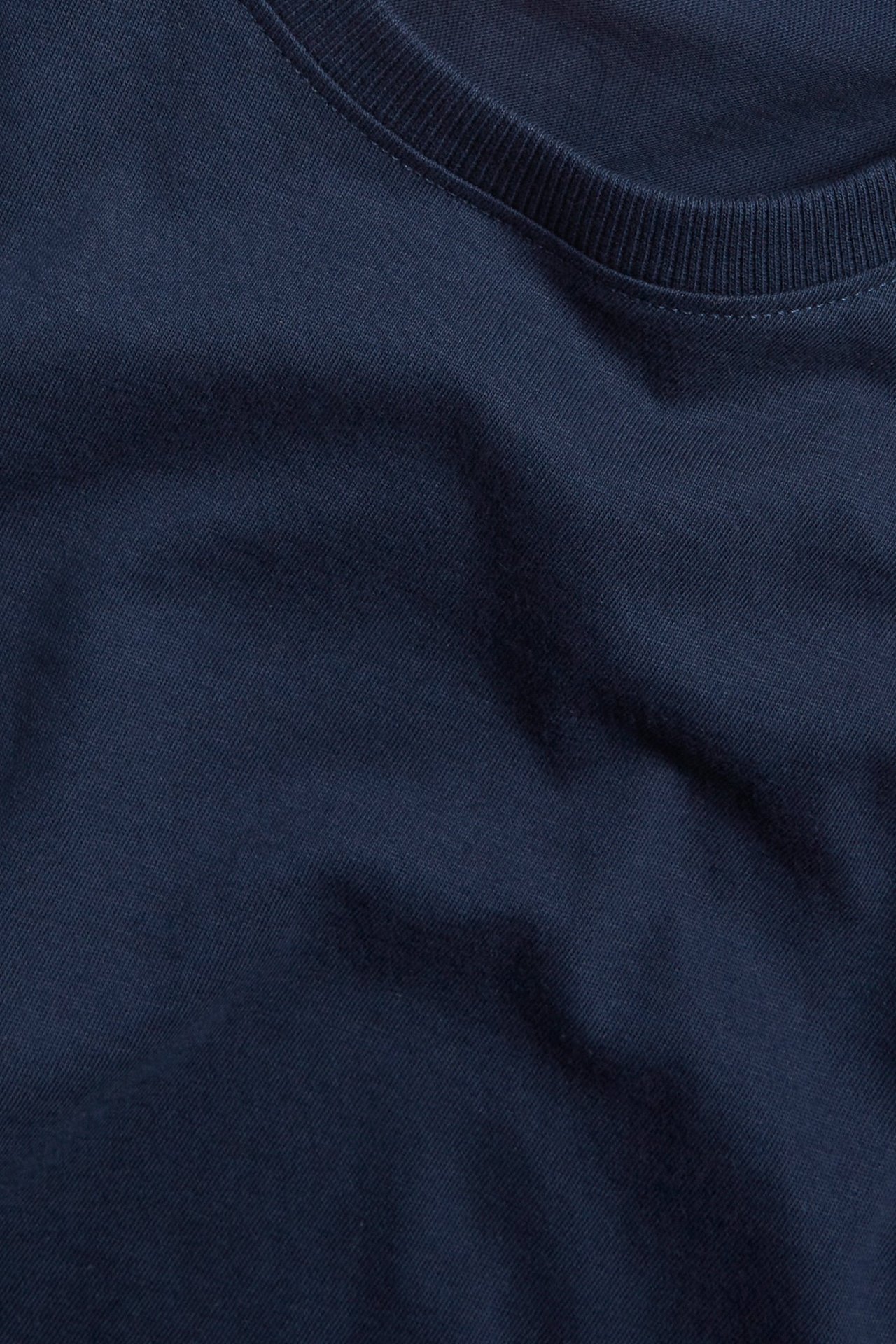 Närbild av en mörkblå enfärgad bomulls-t-shirt med ribbad rundhals.