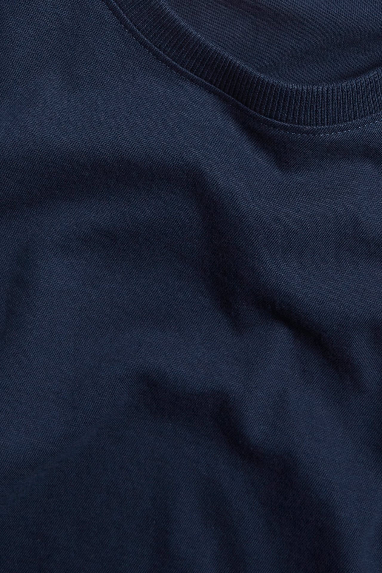 Närbild av en mörkblå enfärgad T-shirt i bomull med ribbad rund hals.