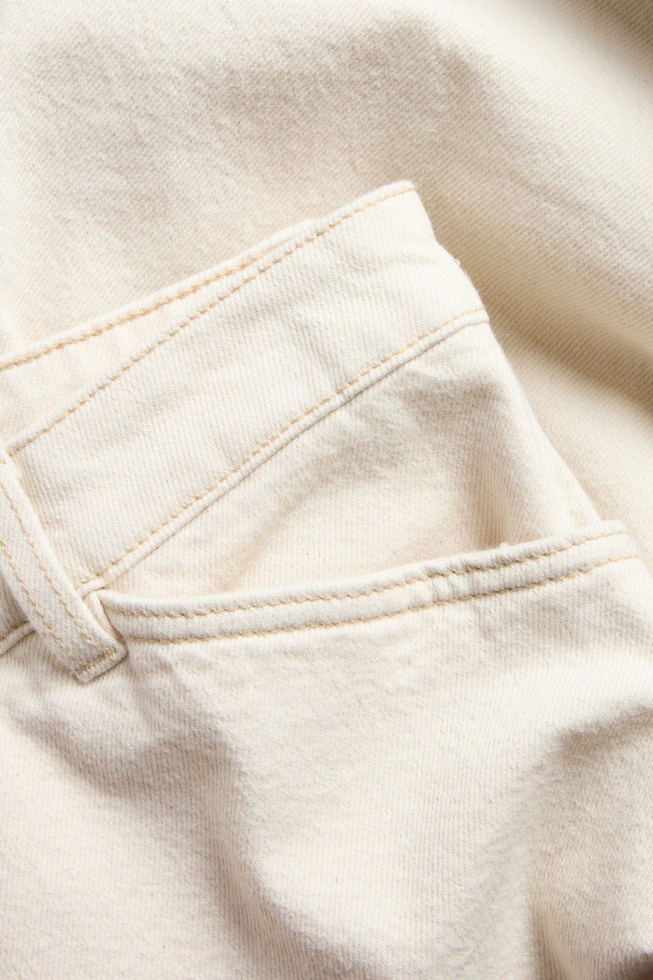 Nærbilde av beige twillbukser som viser lommeåpning, beltestropp og kontrastsømmer.