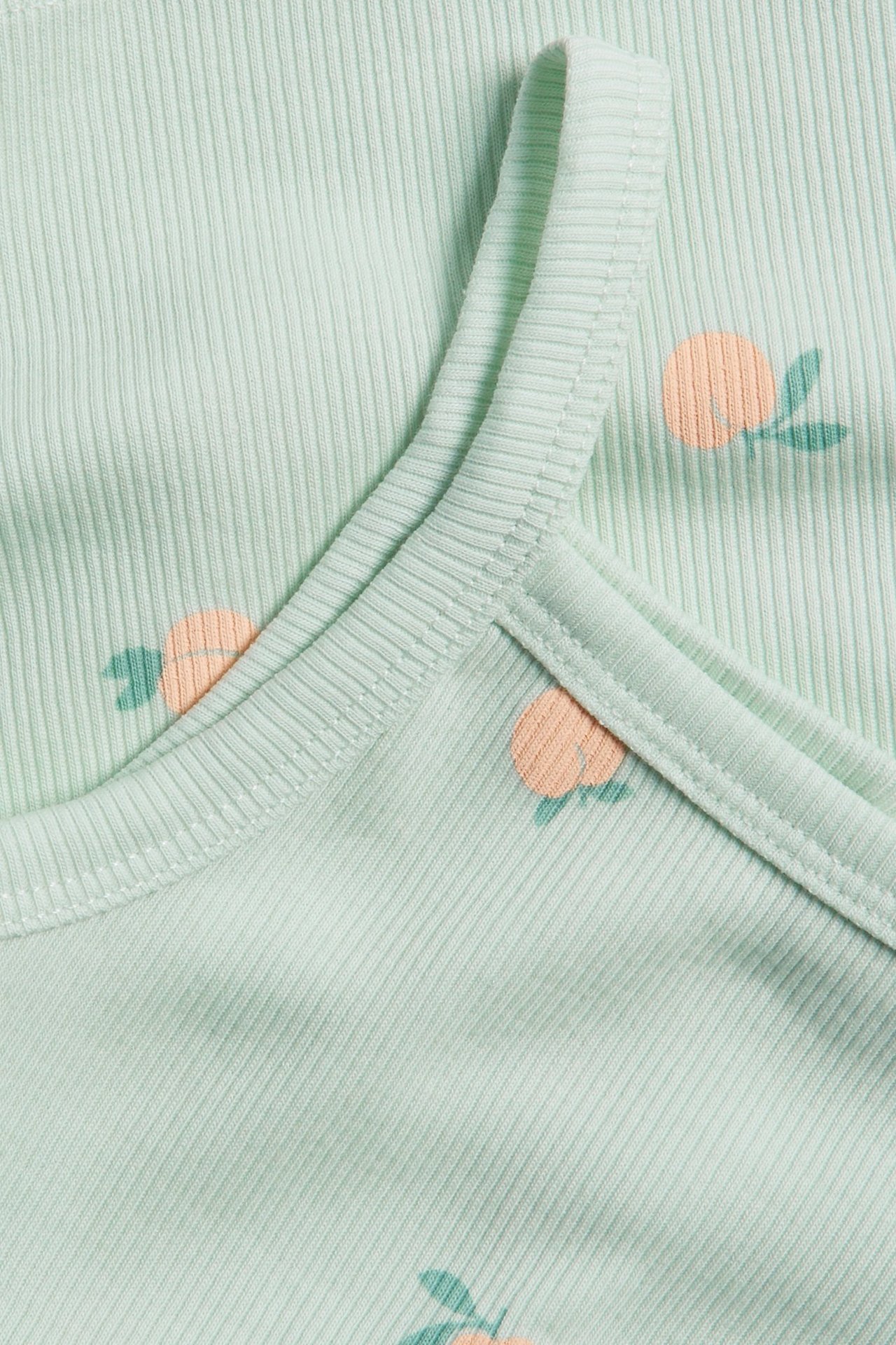 Zbliżenie na jasnozielony prążkowany top z nadrukiem brzoskwiń.