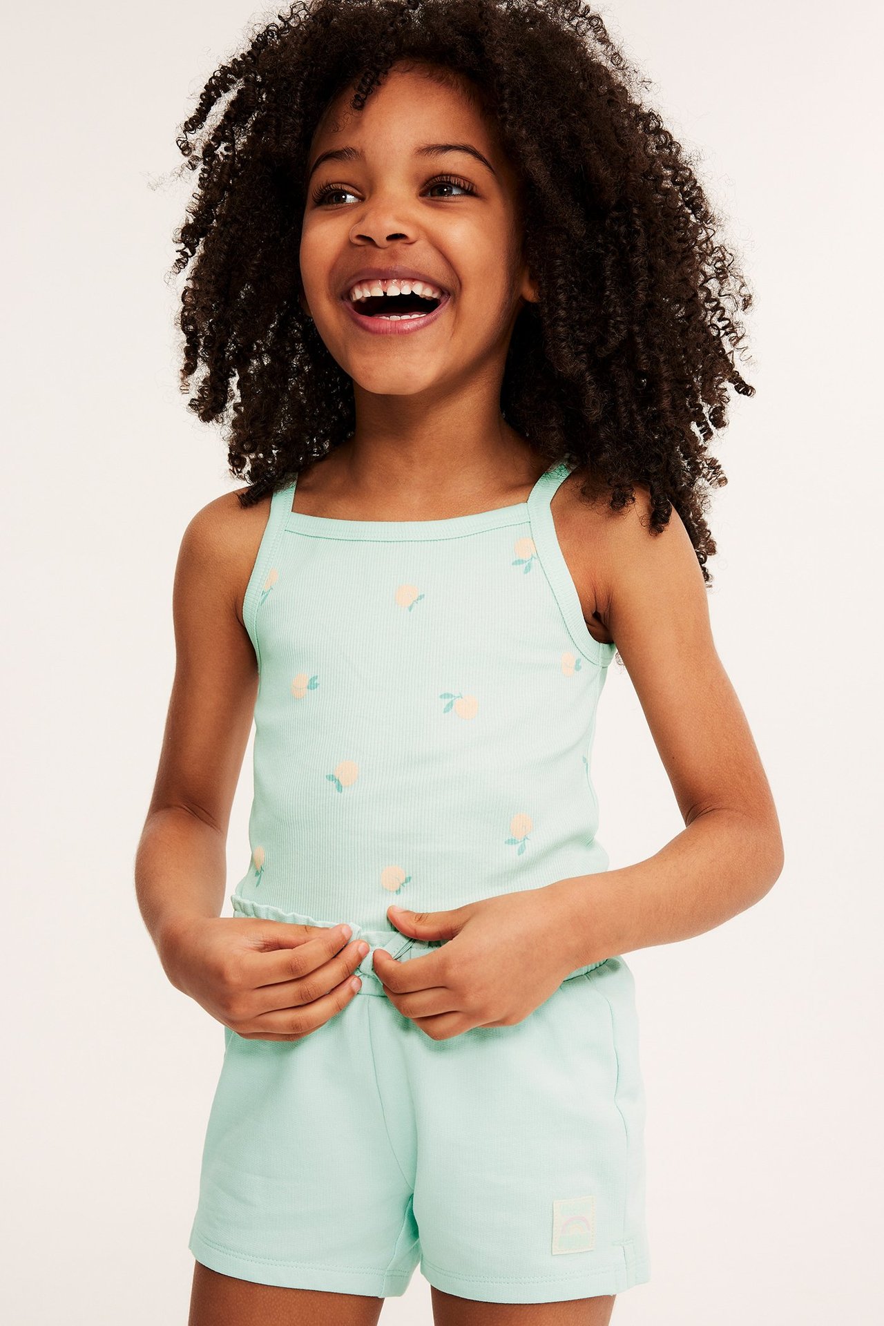 Widok z przodu: dziecko w jasnozielonym prążkowanym topie z brzoskwiniowym wzorem i pasujących szortach.