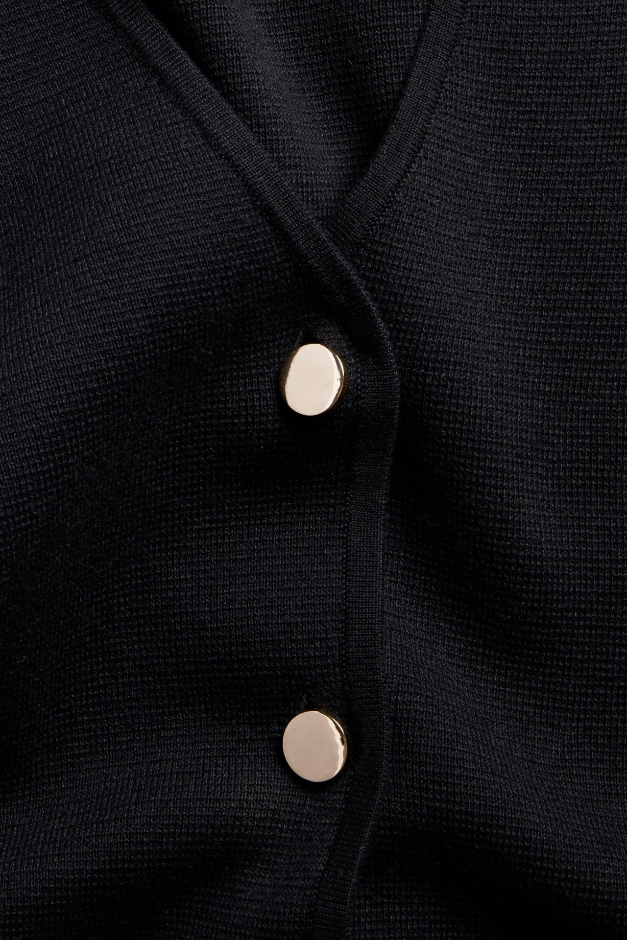 Lähikuva mustasta neulepaidasta, jossa on V-pääntie ja kaksi pyöreää kullanväristä nappia.