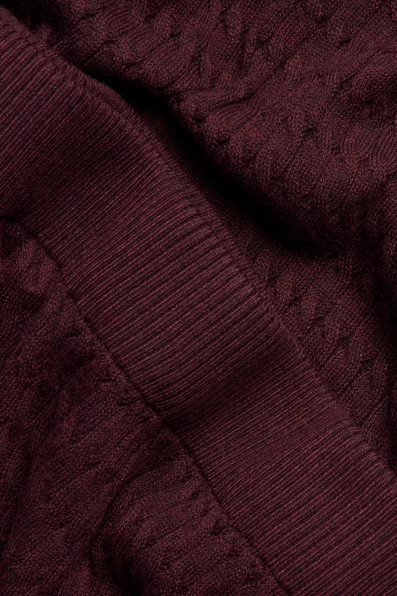 Zbliżenie na bordowy materiał z warkoczowym splotem i prążkowanymi detalami.