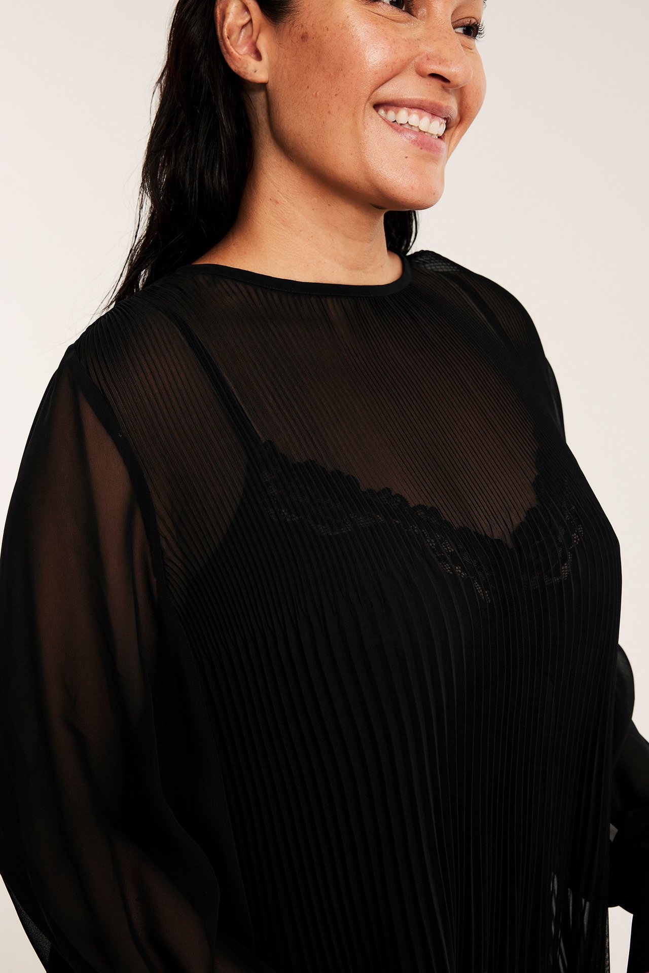Kvinnlig modell i svart, A-linjeformad, plisserad chiffonklänning med luftig design.