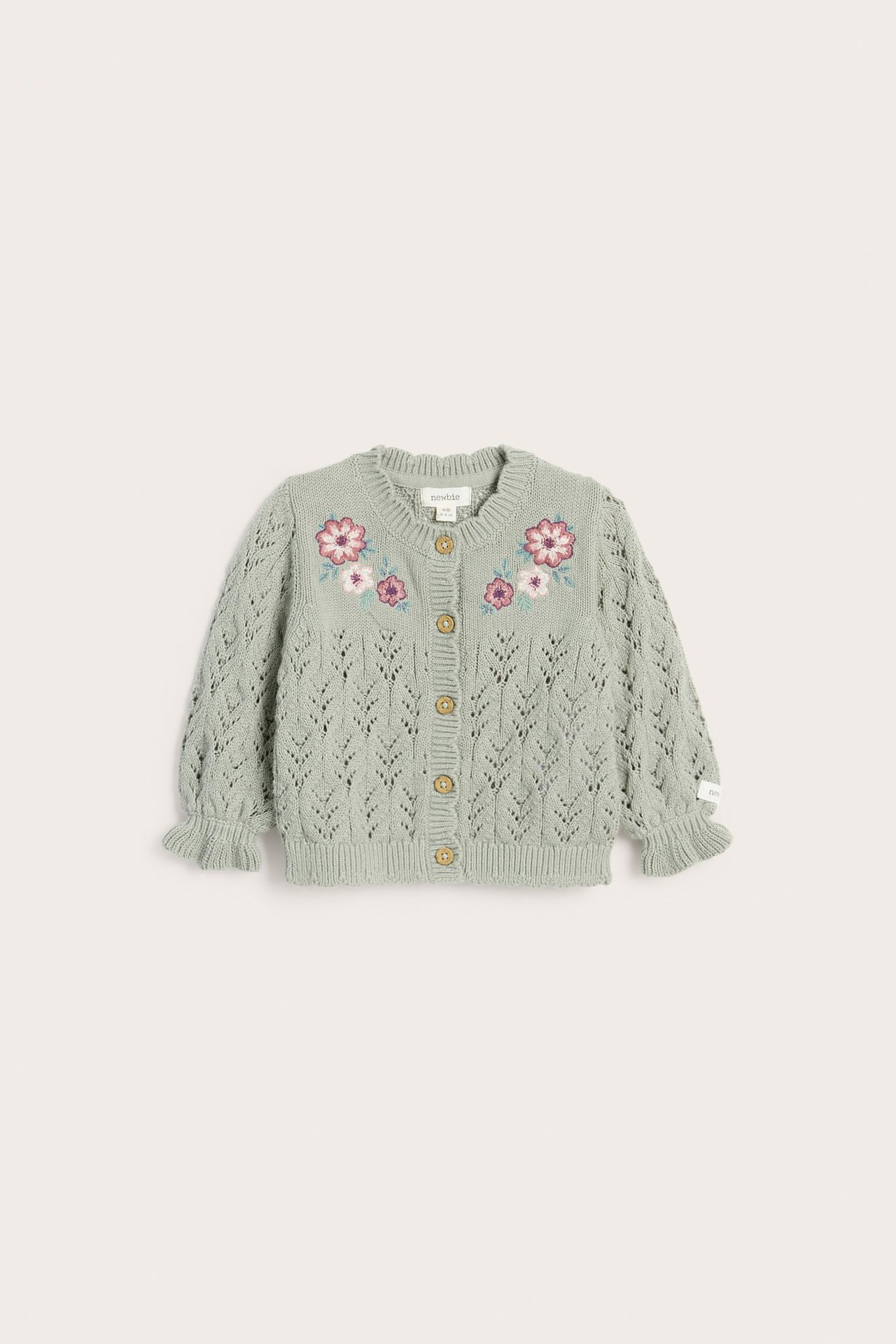 Frontvy av en grön mönsterstickad kofta i bomull med blombroderier, volangärmslut och träknappar.
