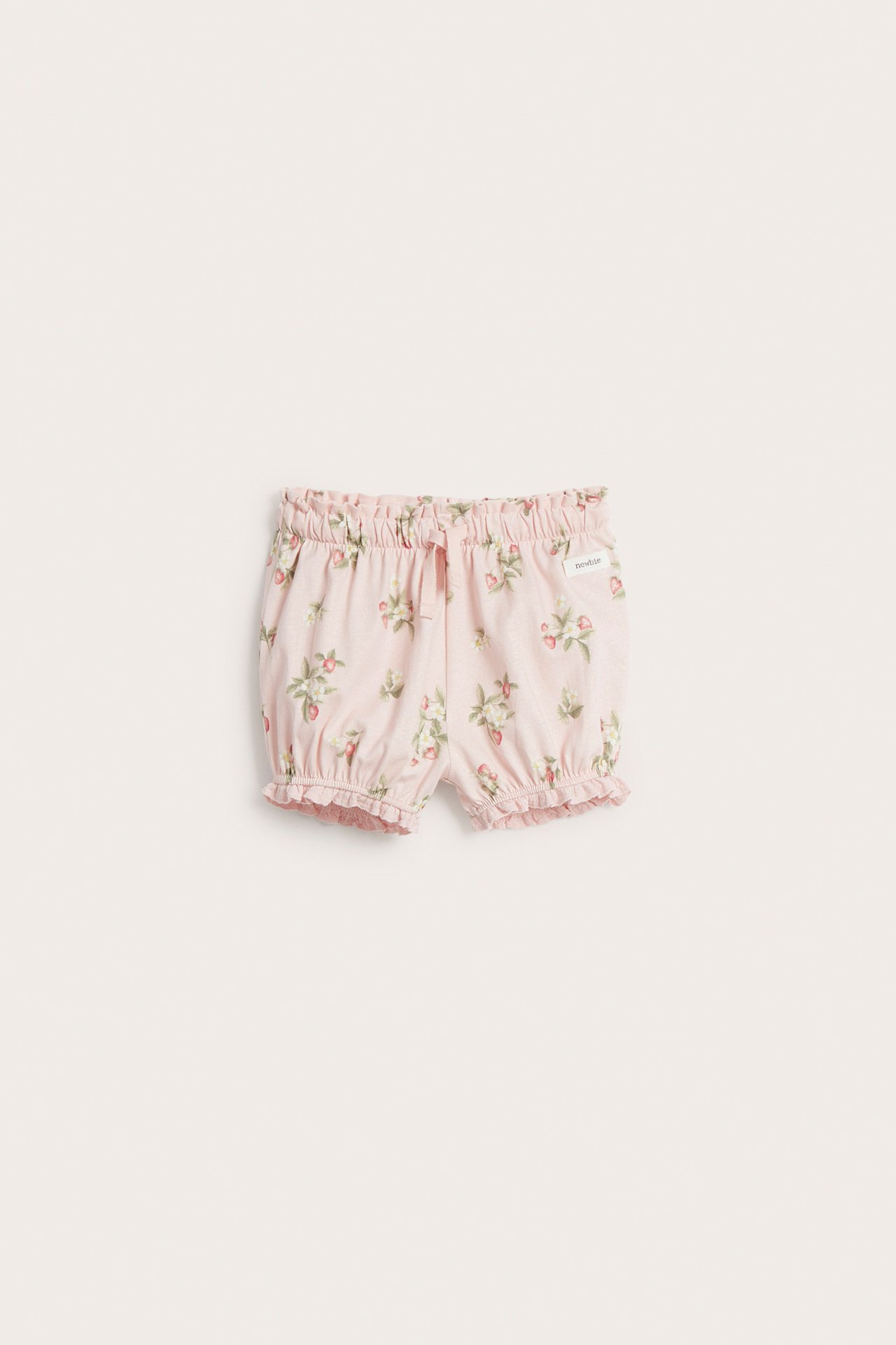 Frontvisning av lyserosa baby shorts med jordbærmønster, elastisk midje, snøring og volanger ved benåpningene.