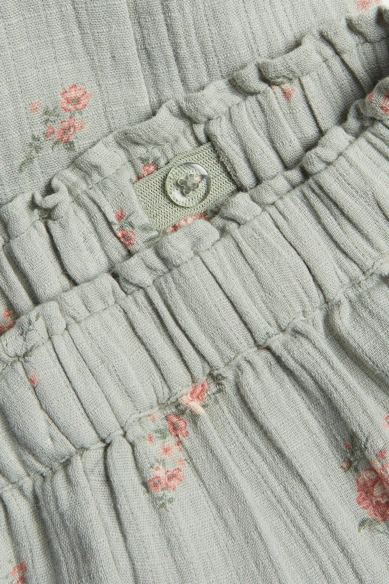 Zbliżenie zielonych, kwiecistych, tkanych spodni bawełnianych z elastyczną talią i regulowanym guzikiem.