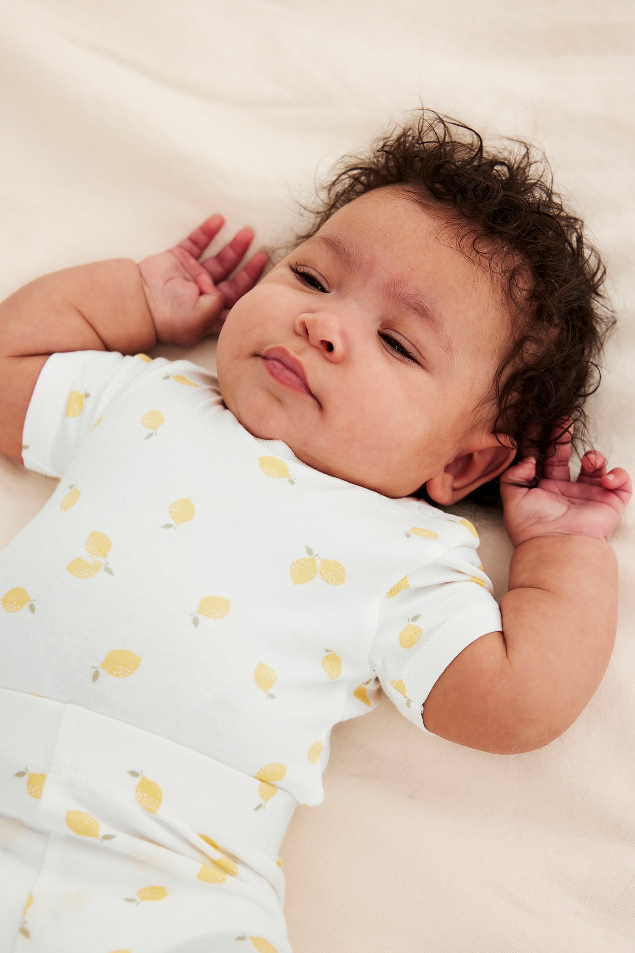 Närbild på en baby i en offwhite kortärmad body med gult citronmönster.